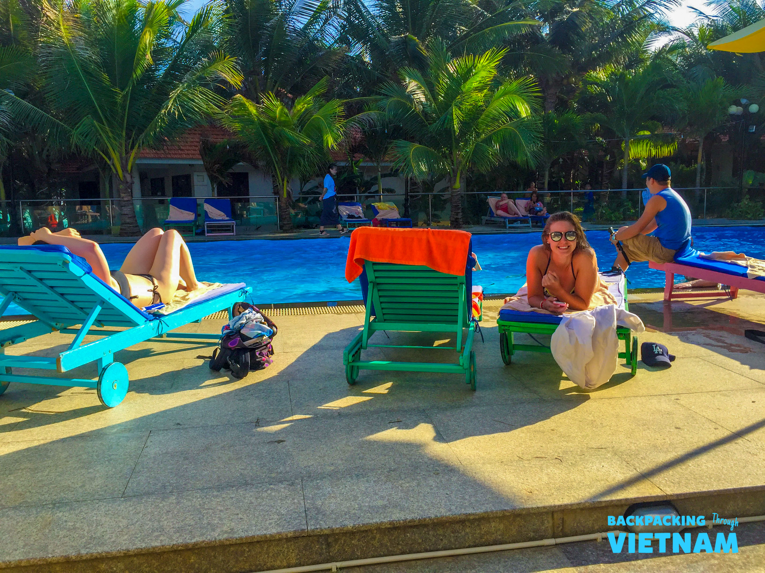 Travelers relax by the vibrant blue swimming pool at a sunny resort in Mui Ne, Vietnam.