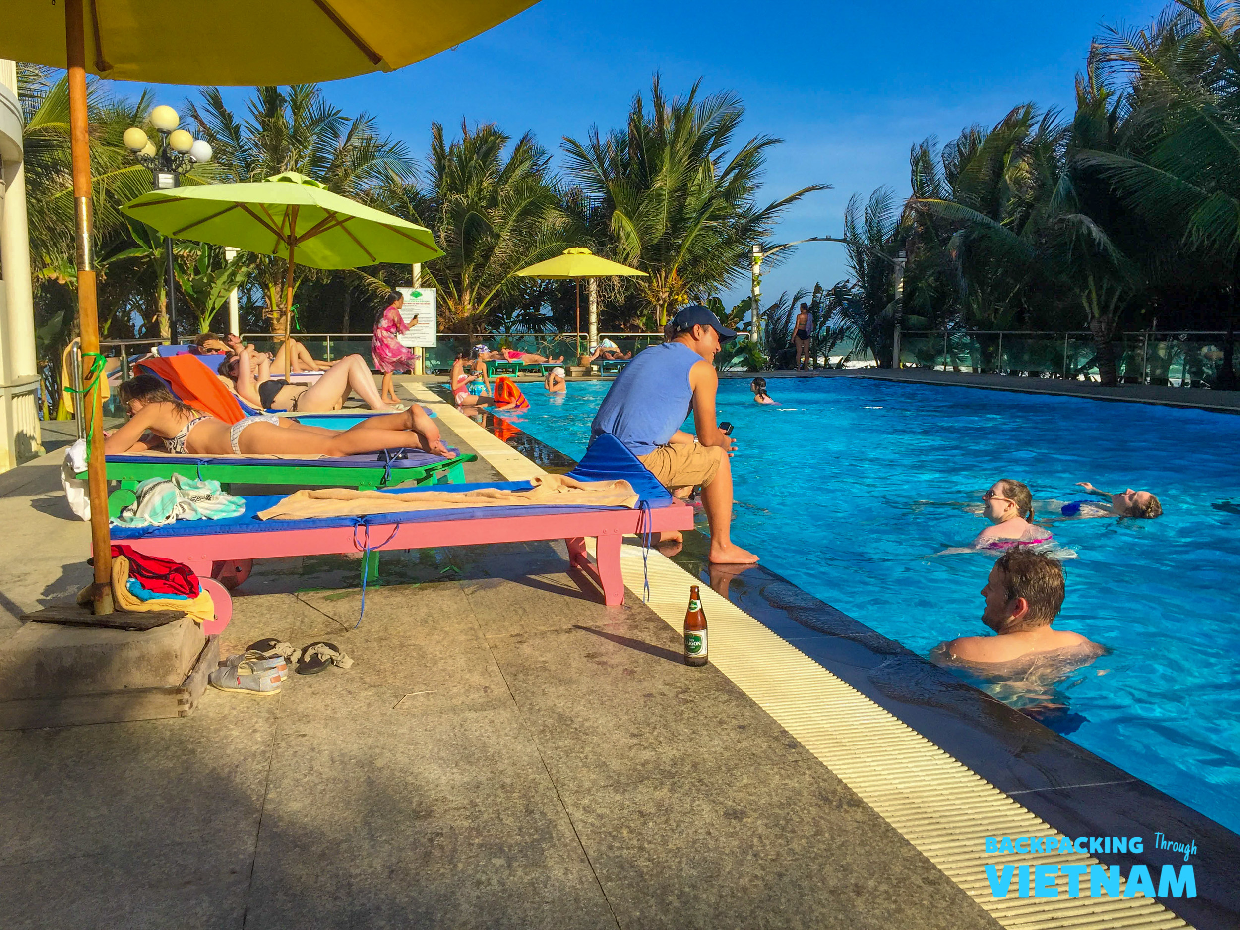 Tourists relax by the sunny swimming pool at a beautiful beach resort in Mui Ne, Vietnam.