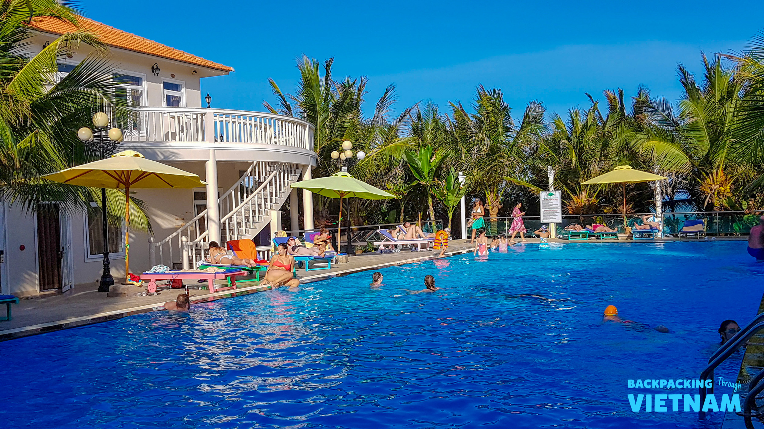 Guests relax and swim in the large blue swimming pool at a resort in Mui Ne, Vietnam.