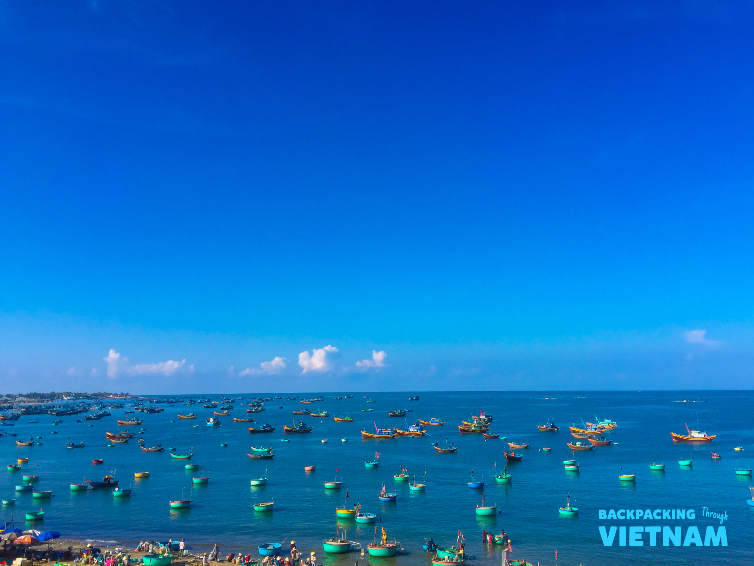 Vibrant fishing boats and basket boats dot the clear blue ocean in Mui Ne, Vietnam.