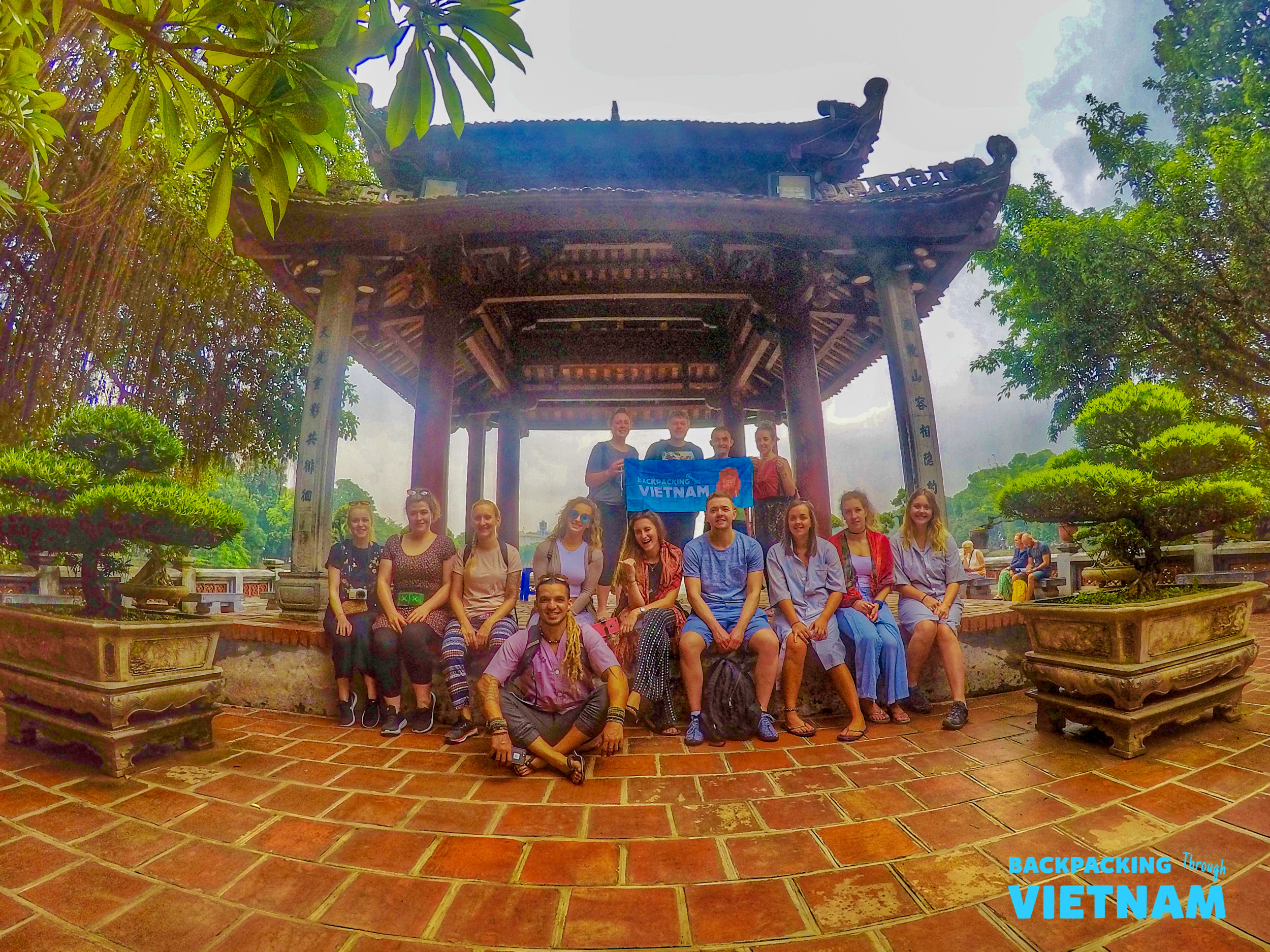 A cheerful group of backpackers poses at a traditional pavilion during their tour of Hanoi.