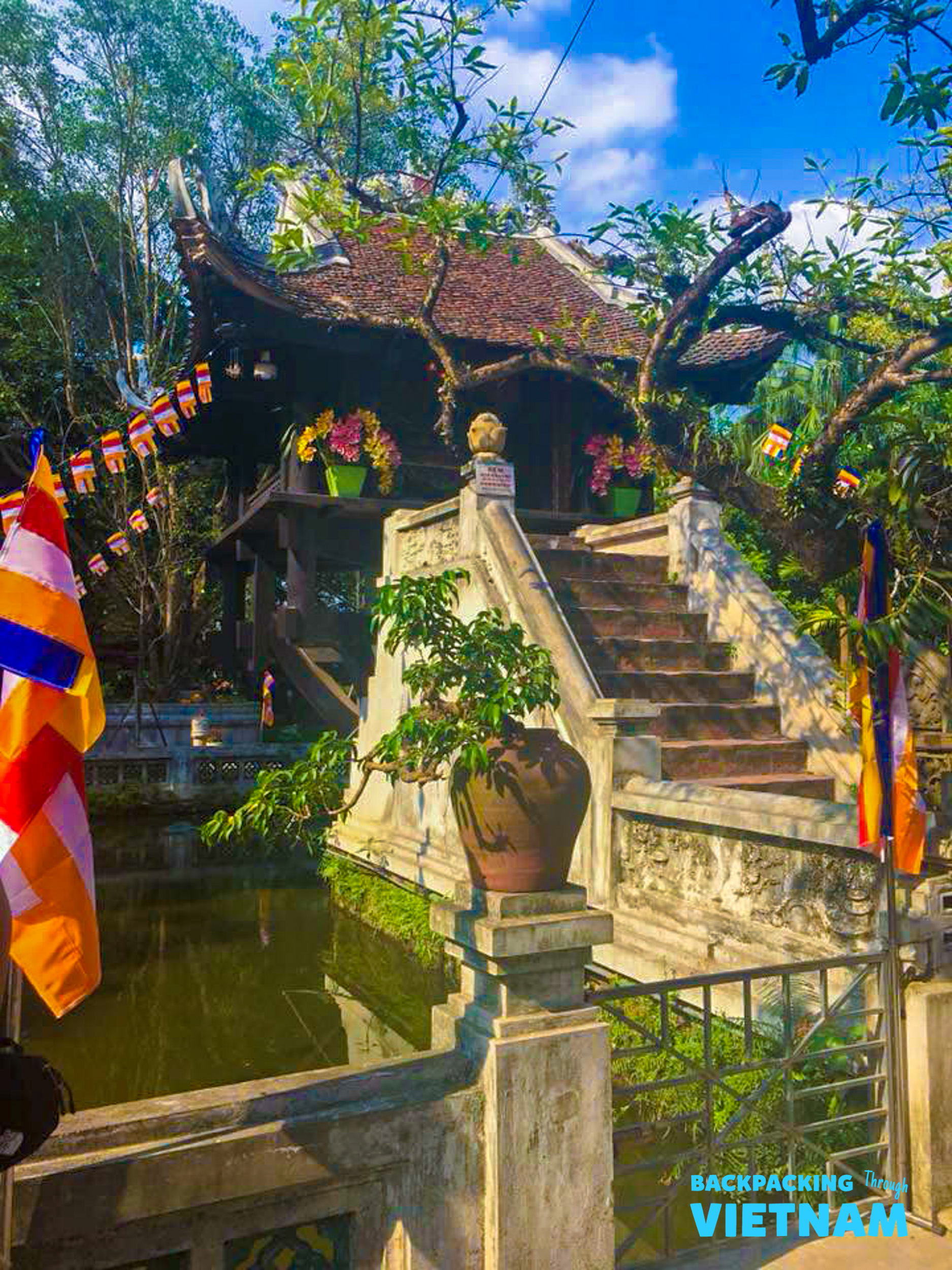 The historic One Pillar Pagoda in Hanoi, with its unique architecture, stairs, and colorful flags over a pond.