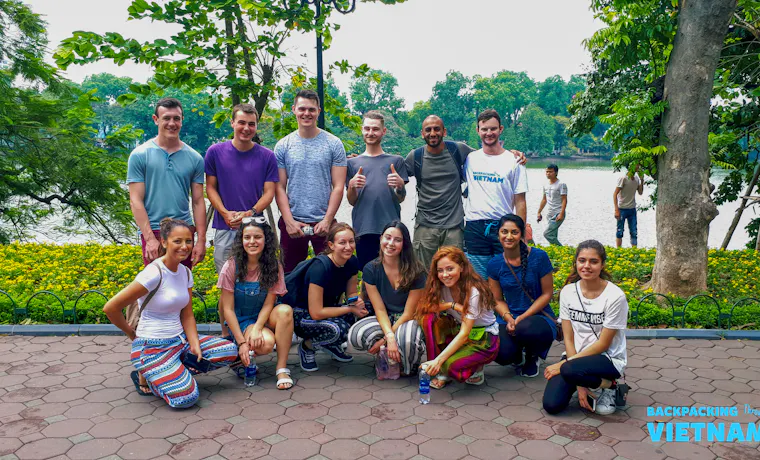 Happy travelers pose for a group photo in a scenic park beside a lake in Hanoi.