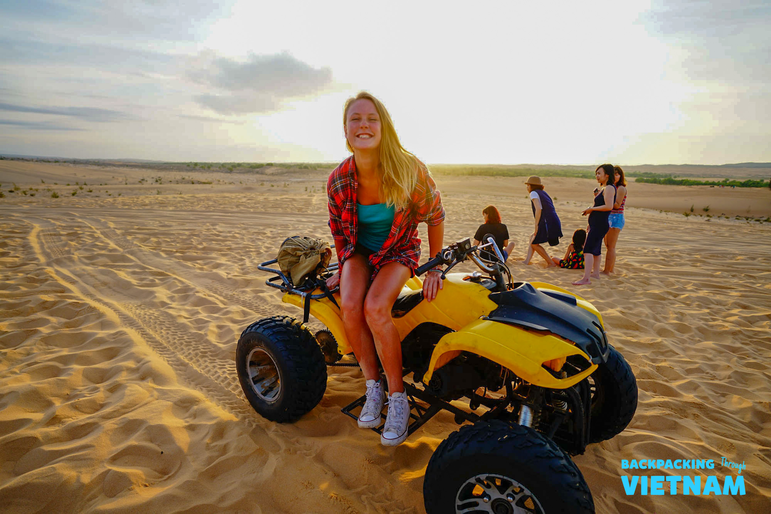Happy woman on a yellow ATV exploring the vast sand dunes of Mui Ne at sunrise.