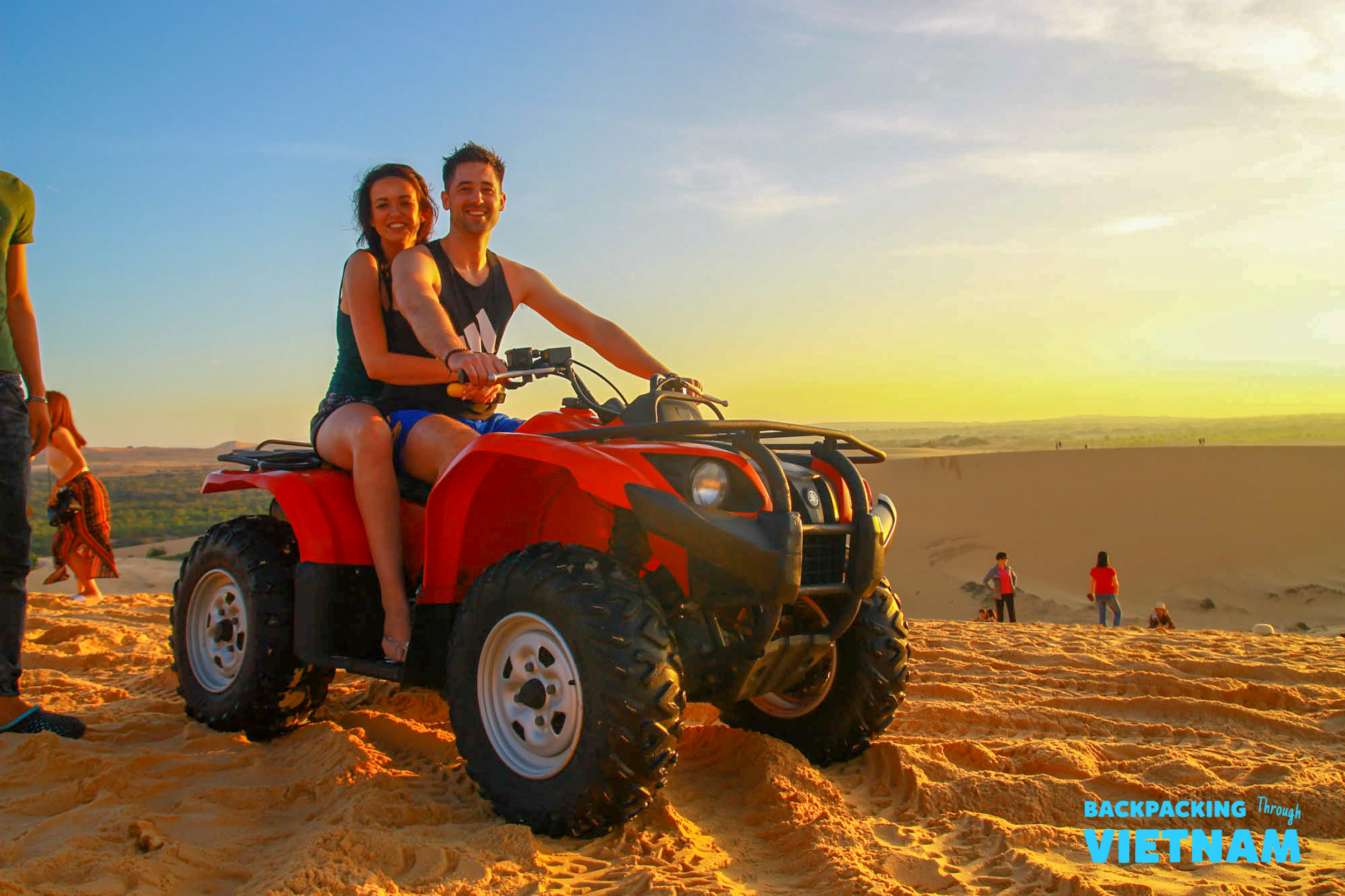 Smiling couple enjoying an adventurous ATV ride on the golden sand dunes of Mui Ne, Vietnam.