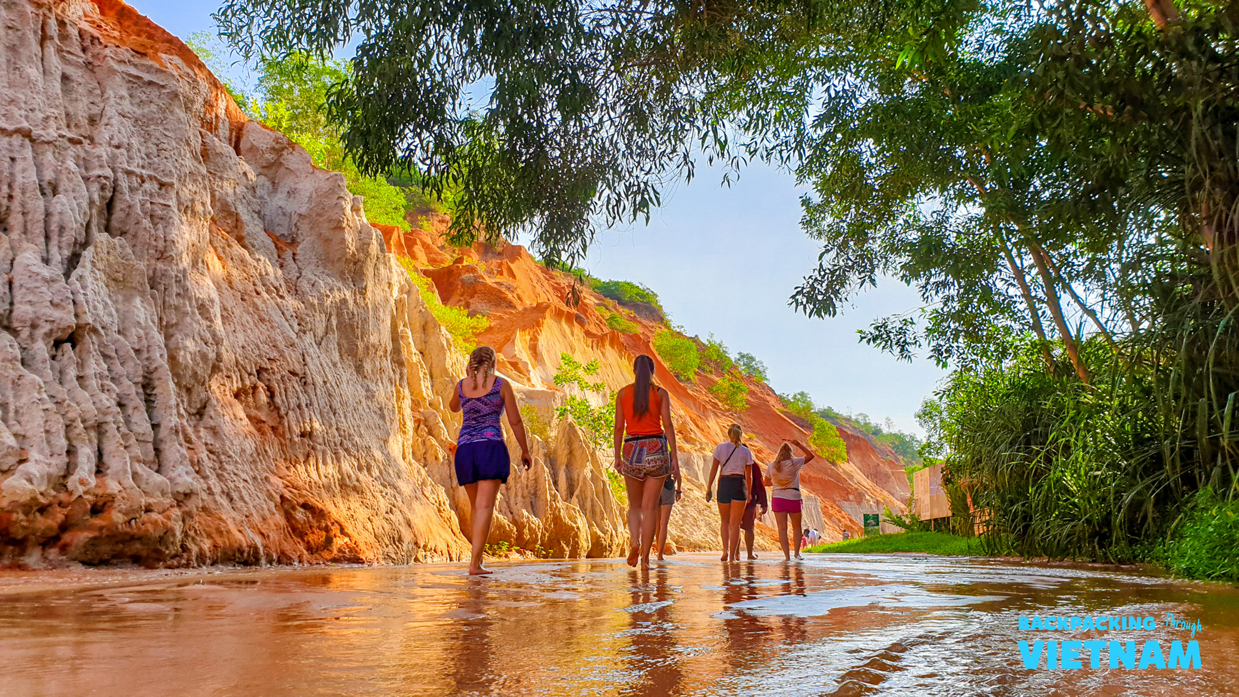 Four women walk through the enchanting Fairy Stream in Mui Ne, surrounded by colorful canyon walls.
