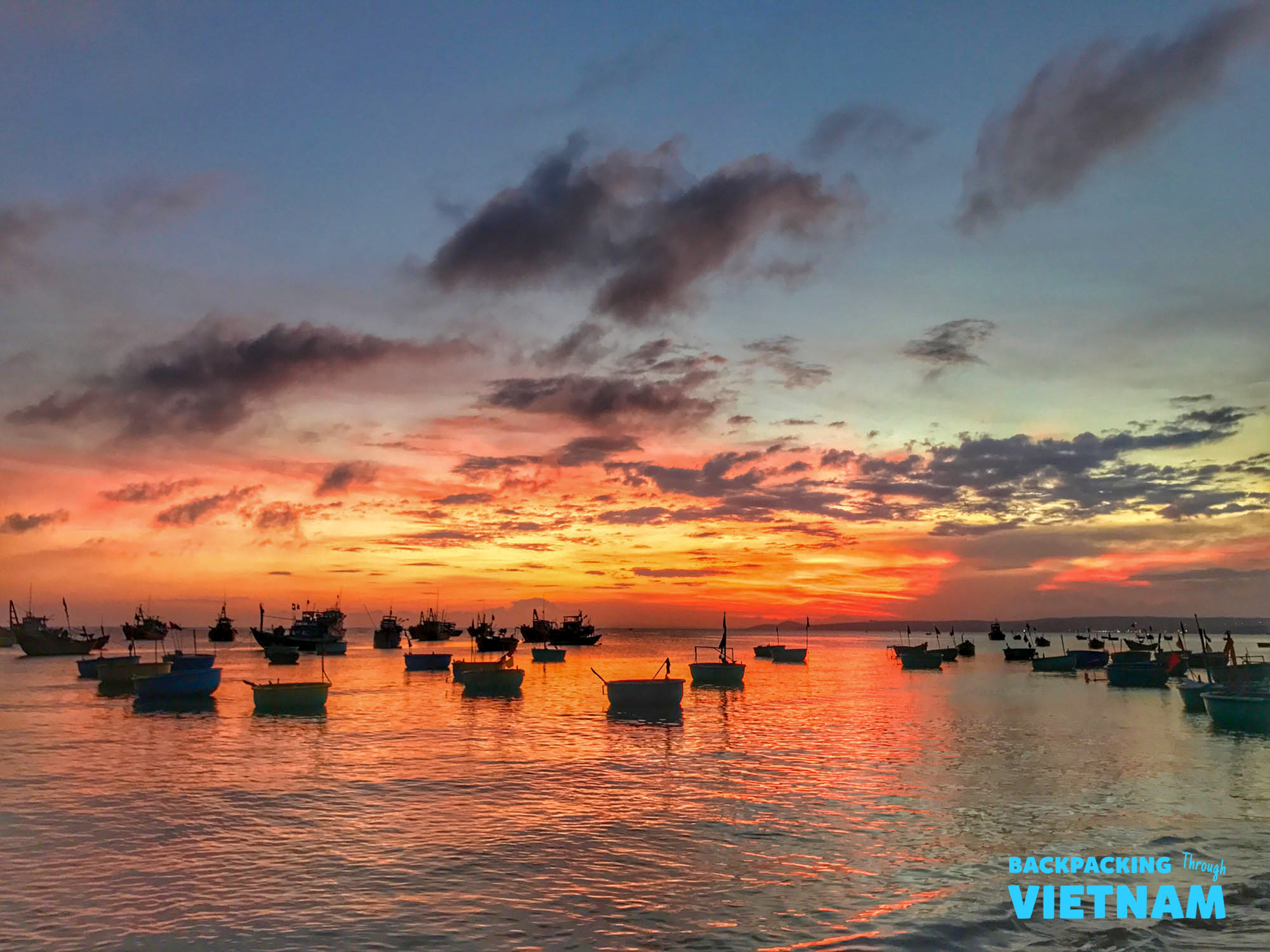 Vibrant sunset over Mui Ne bay, with fishing boats and traditional basket boats reflecting the colors.