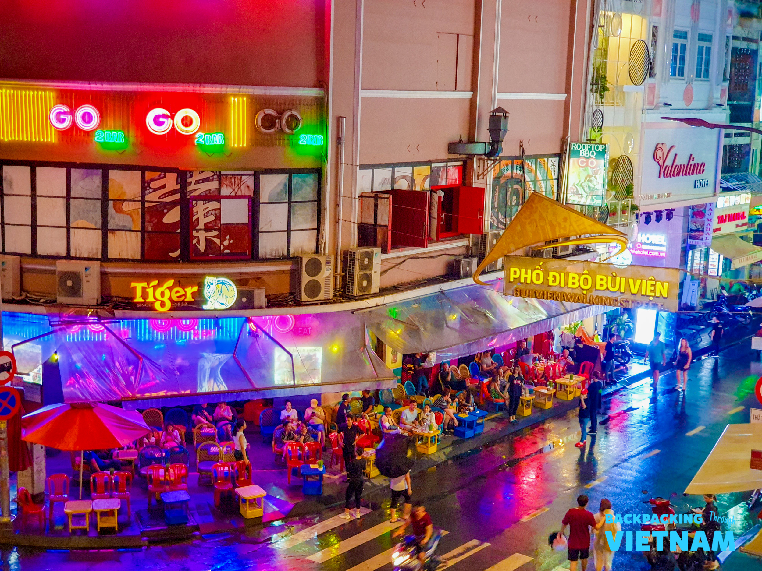 Bustling Bui Vien Walking Street at night, with people enjoying drinks under colorful neon lights.