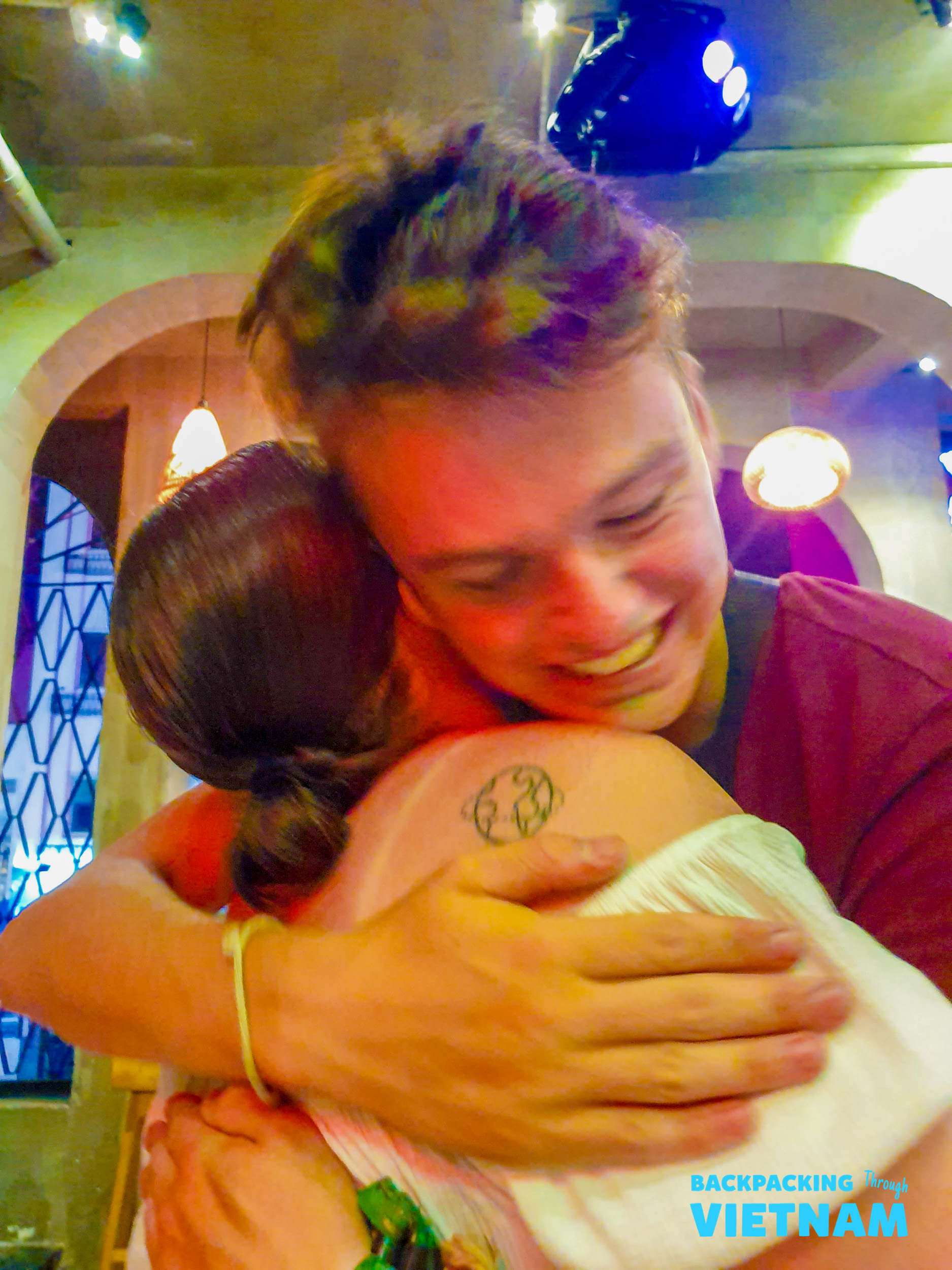 A smiling male traveler embraces a friend, sharing a warm farewell hug in Hoi An.