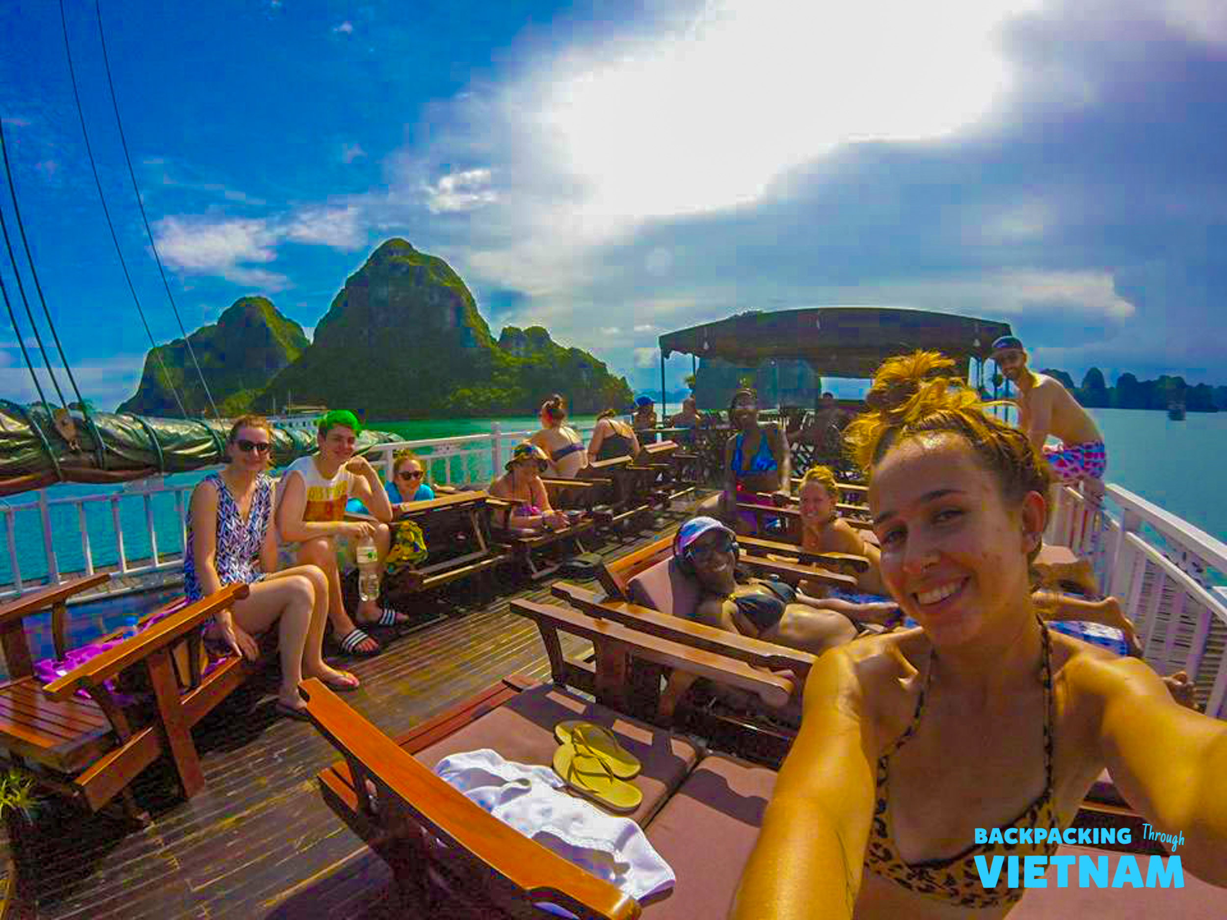 Happy backpackers take a selfie on a boat deck, cruising through the stunning Halong Bay.