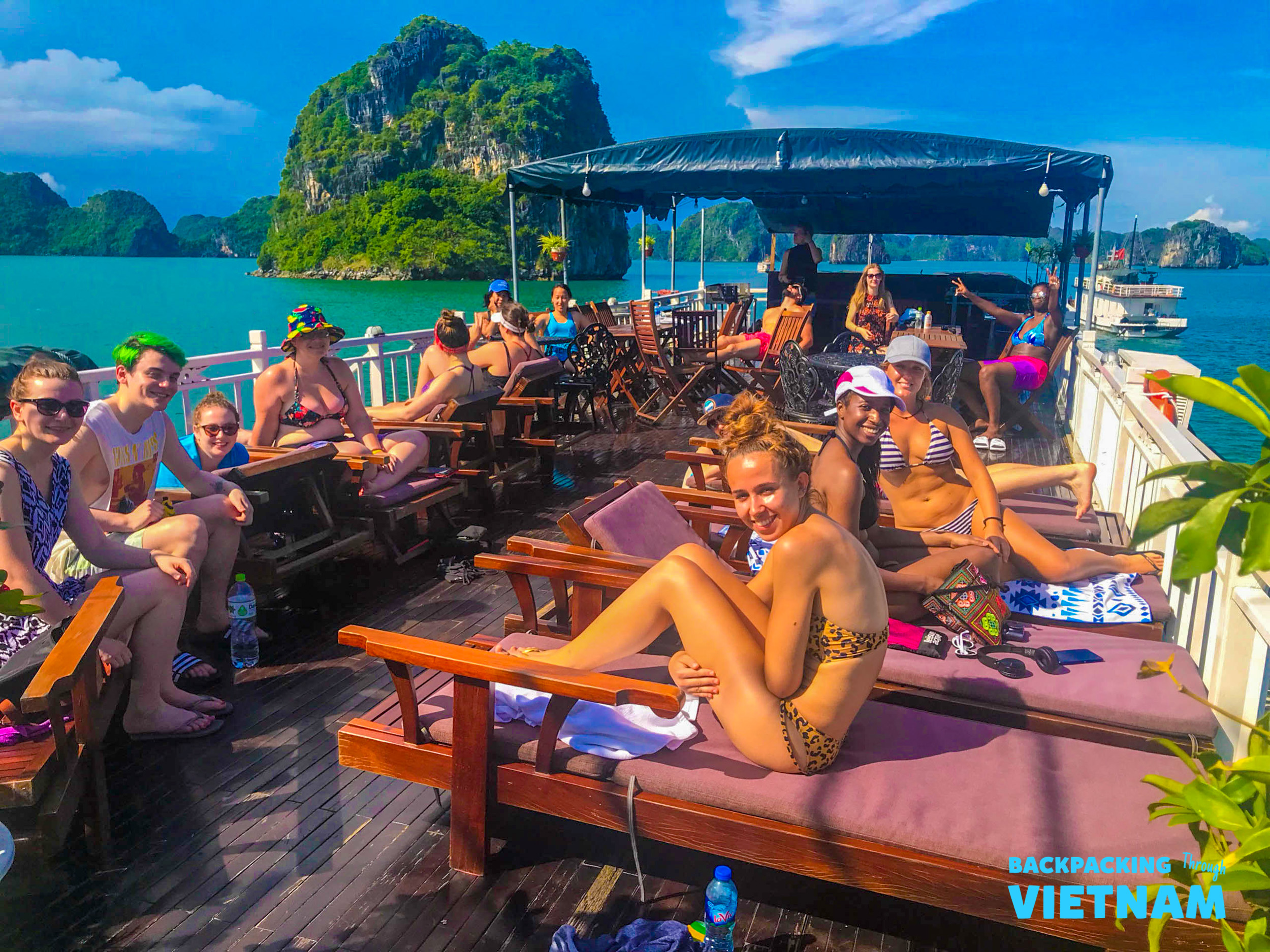 Happy backpackers relax on a boat deck, cruising through the stunning limestone karsts of Halong Bay.