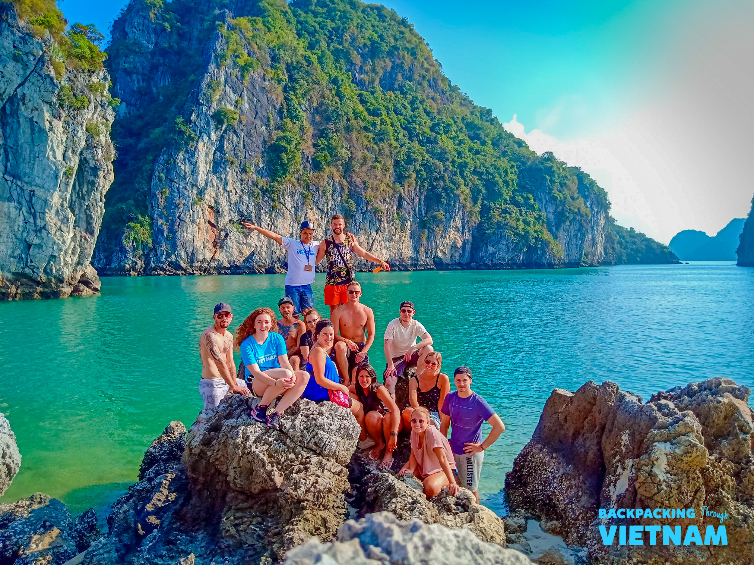 A group of happy backpackers posing on rocks in the beautiful turquoise waters of Halong Bay.