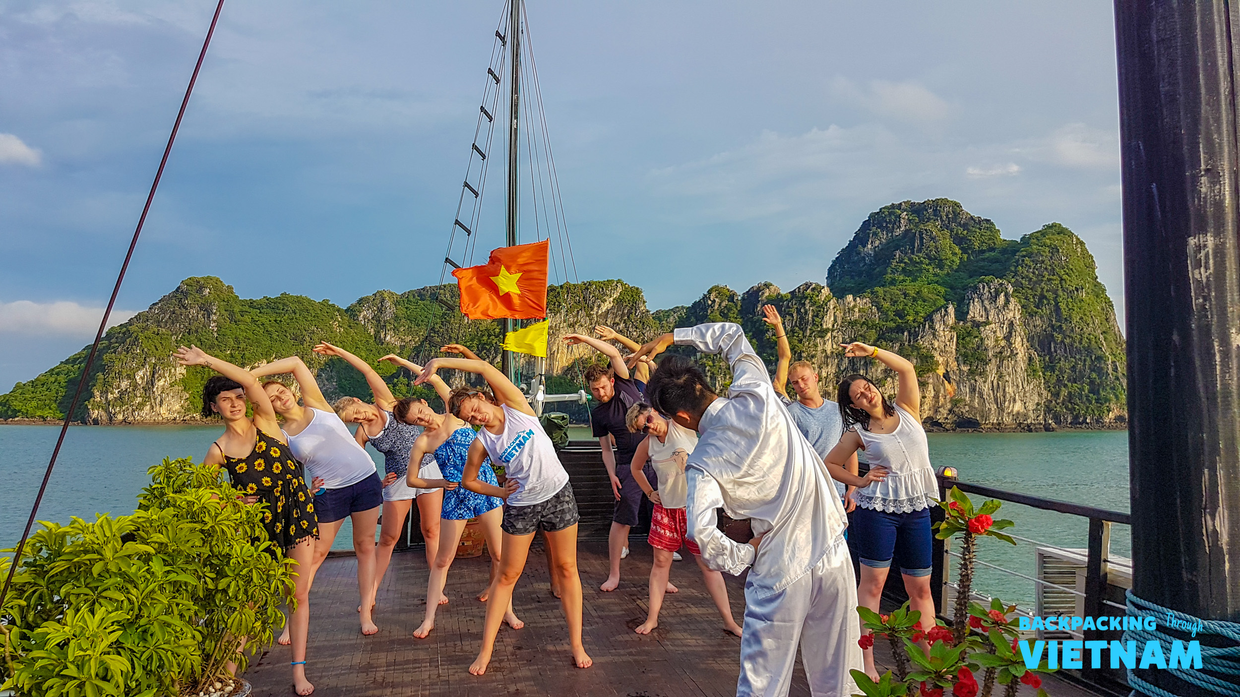 A group enjoys morning yoga on a boat in Vietnam's Halong Bay, with scenic karsts.