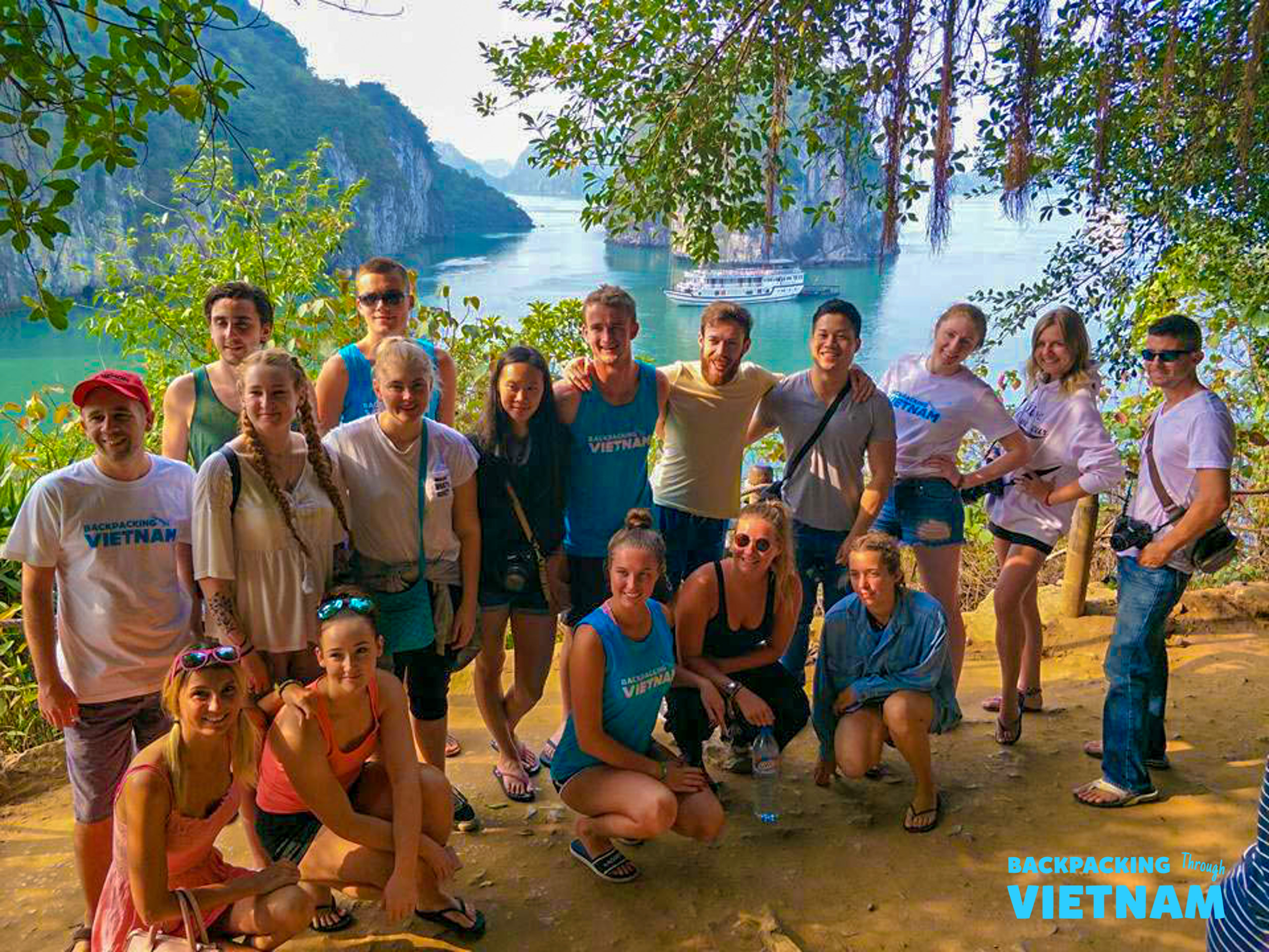 A happy group of backpackers poses with the stunning limestone karsts and emerald waters of Halong Bay.
