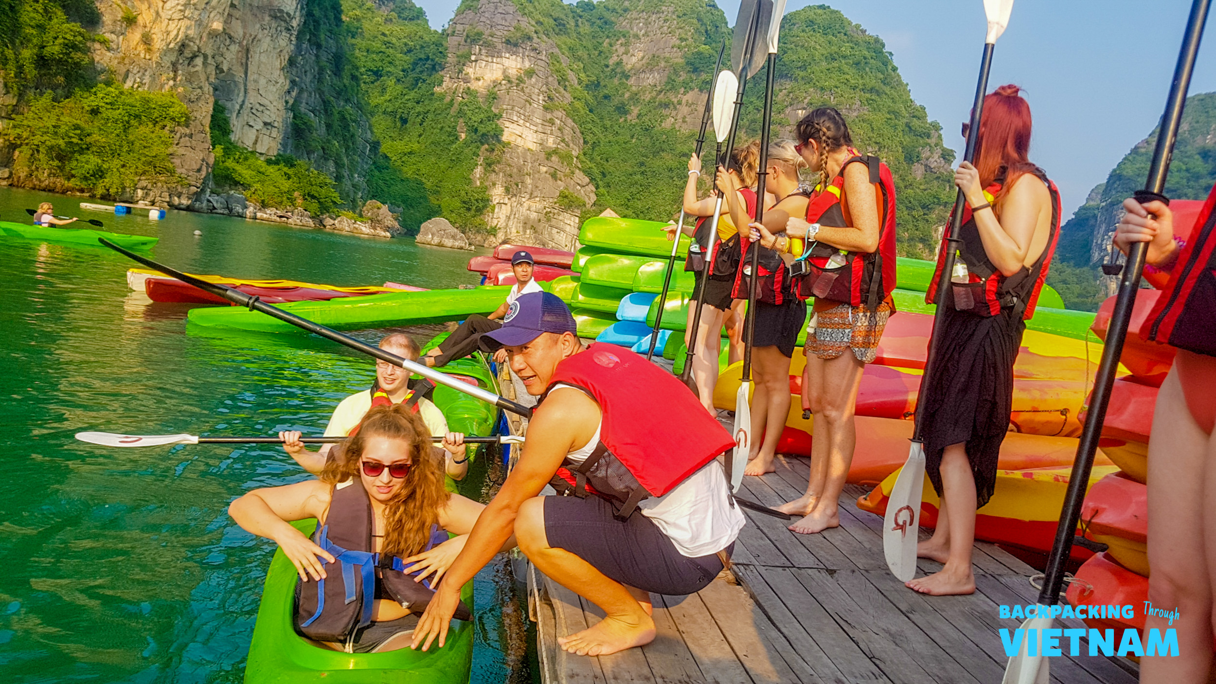 Backpackers in life vests preparing to kayak among the stunning limestone karsts of Halong Bay.
