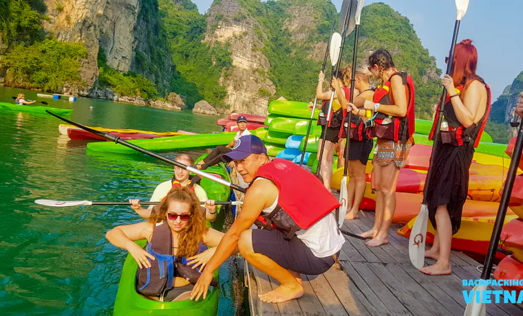 Backpackers in life vests preparing to kayak among the stunning limestone karsts of Halong Bay.