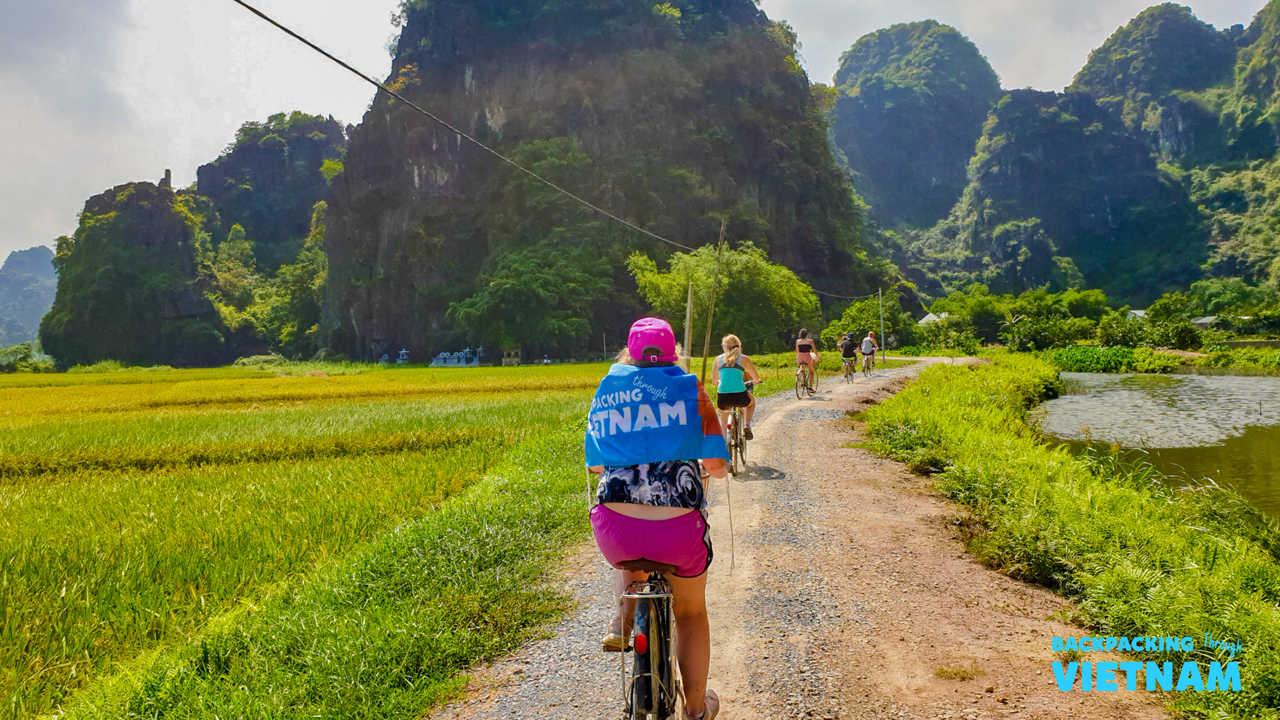 Cyclists enjoy a scenic ride through lush rice fields and dramatic mountains in Tam Coc, Vietnam.
