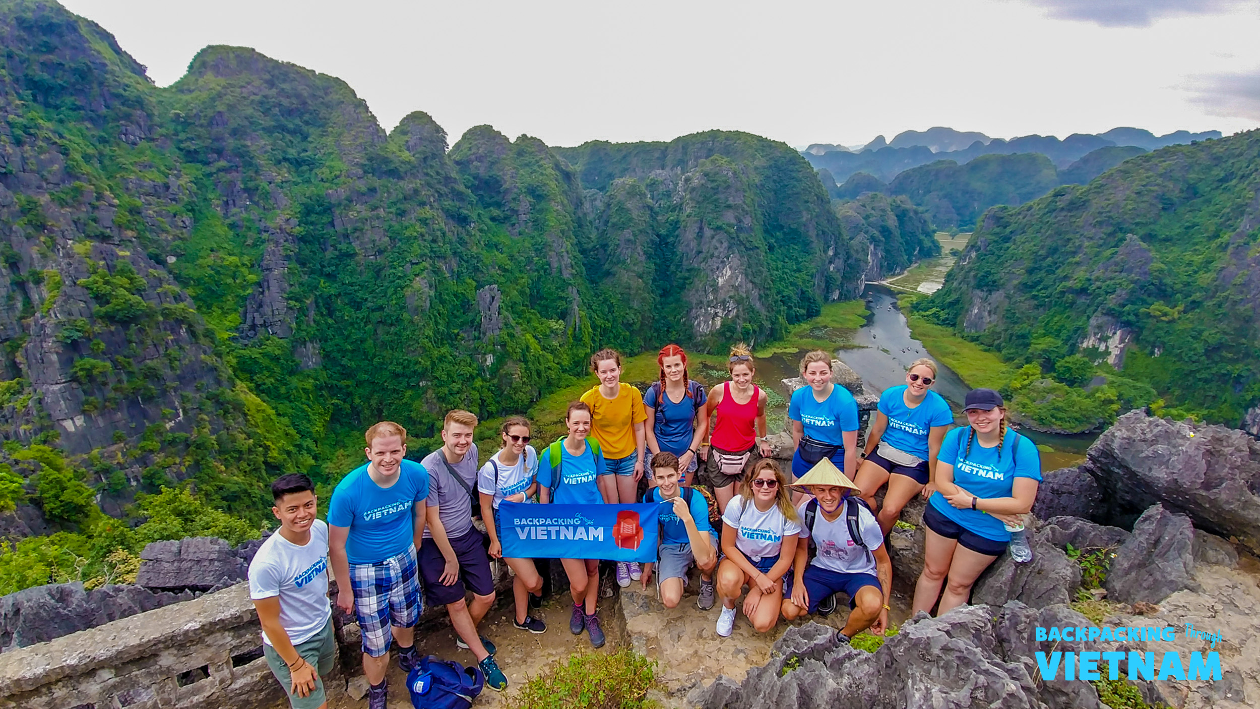 Happy backpackers pose on Lying Dragon Mountain, overlooking the stunning karstic landscape of Tam Coc, Vietnam.
