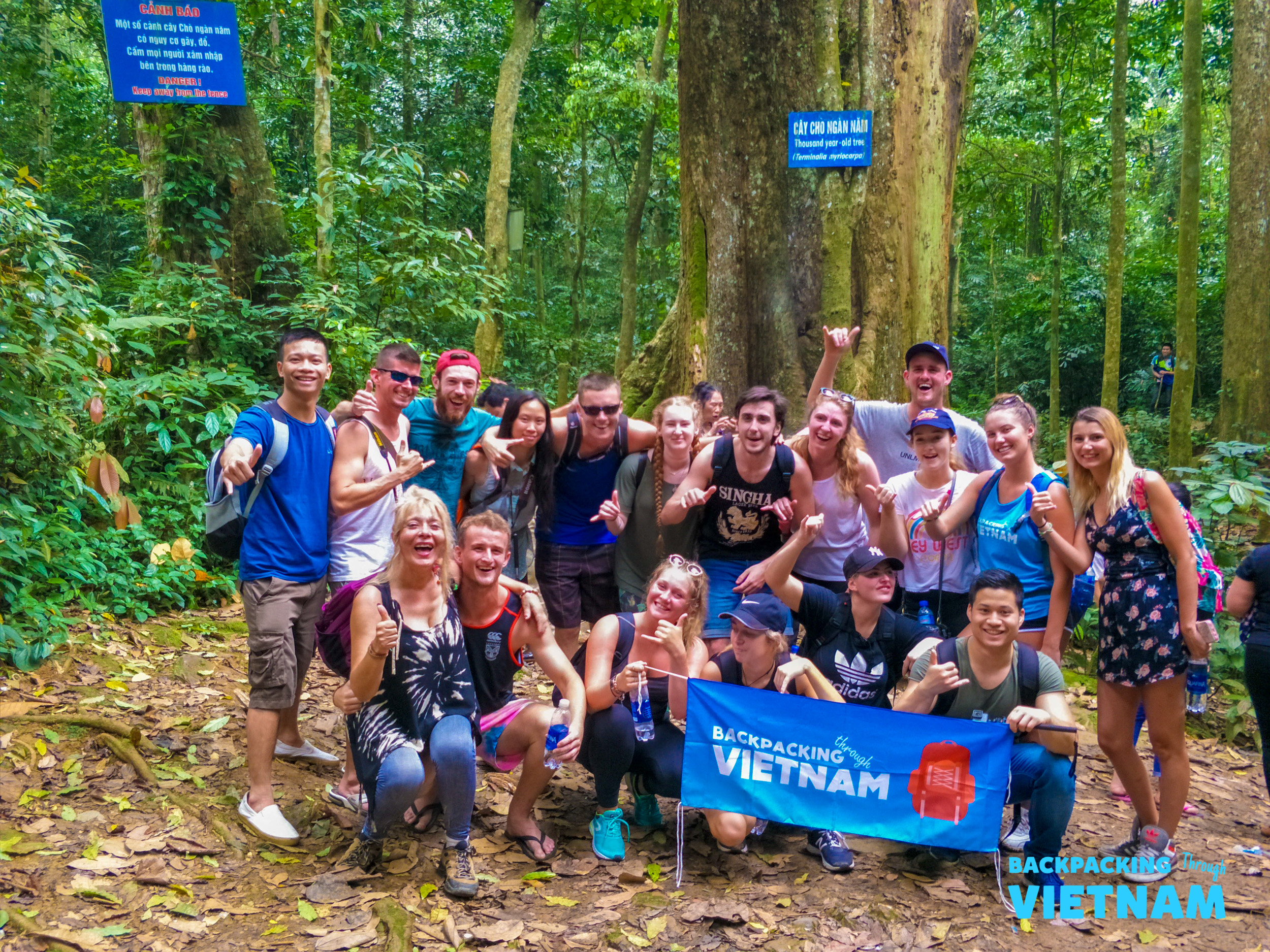 Happy backpackers pose with their Backpacking Vietnam flag during a jungle trek in Phong Nha.