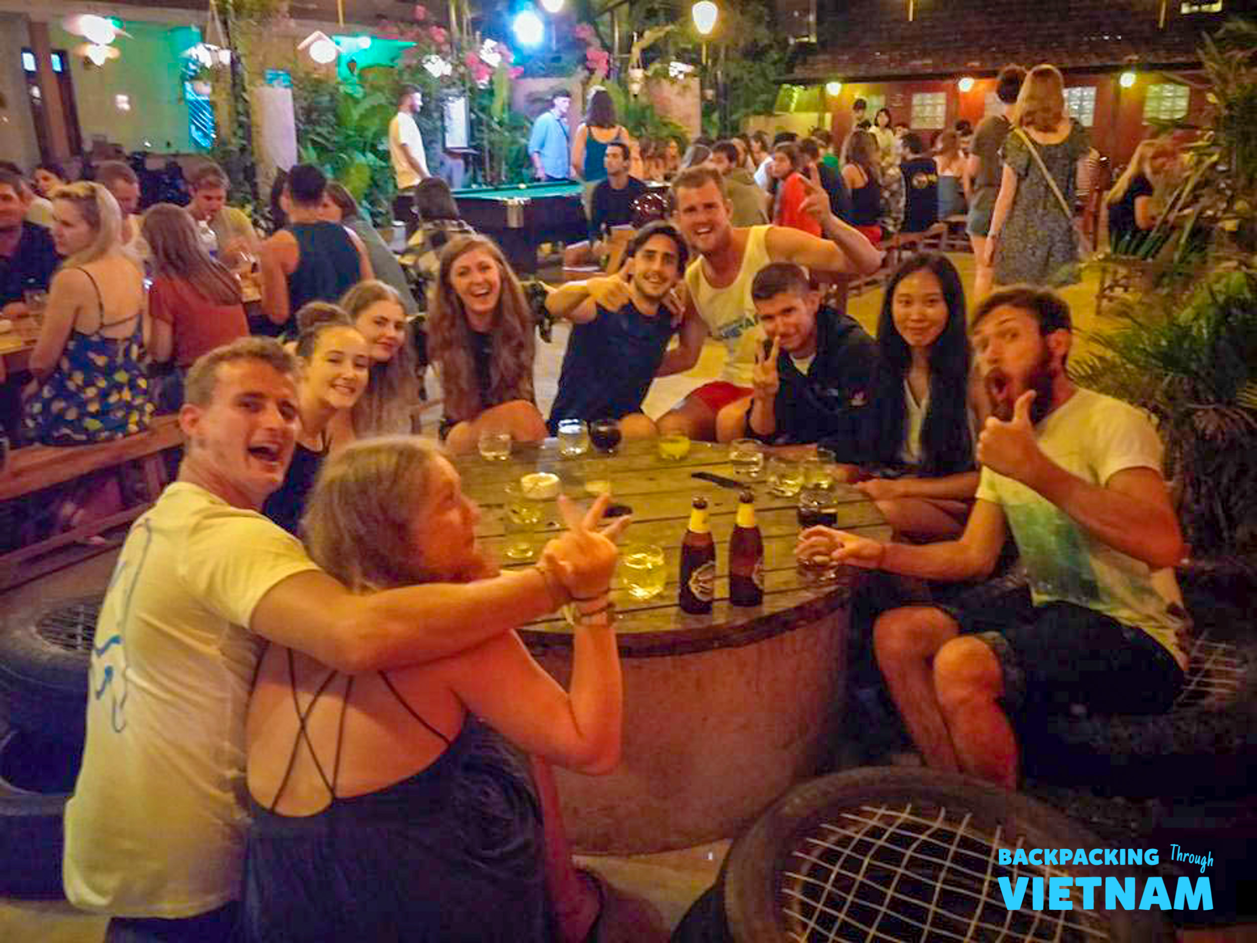 Happy backpackers share drinks and laughter at a vibrant outdoor bar in Phong Nha, Vietnam.