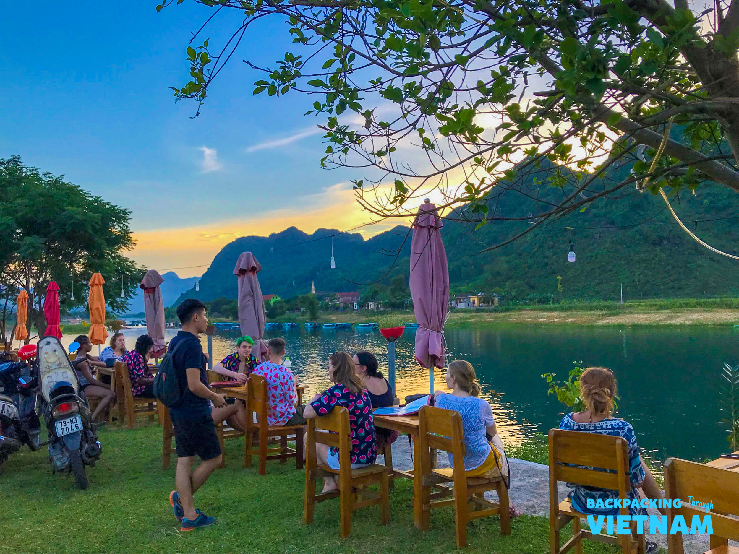 Travelers relax by the river in Phong Nha, enjoying the sunset over the dramatic karst mountains.