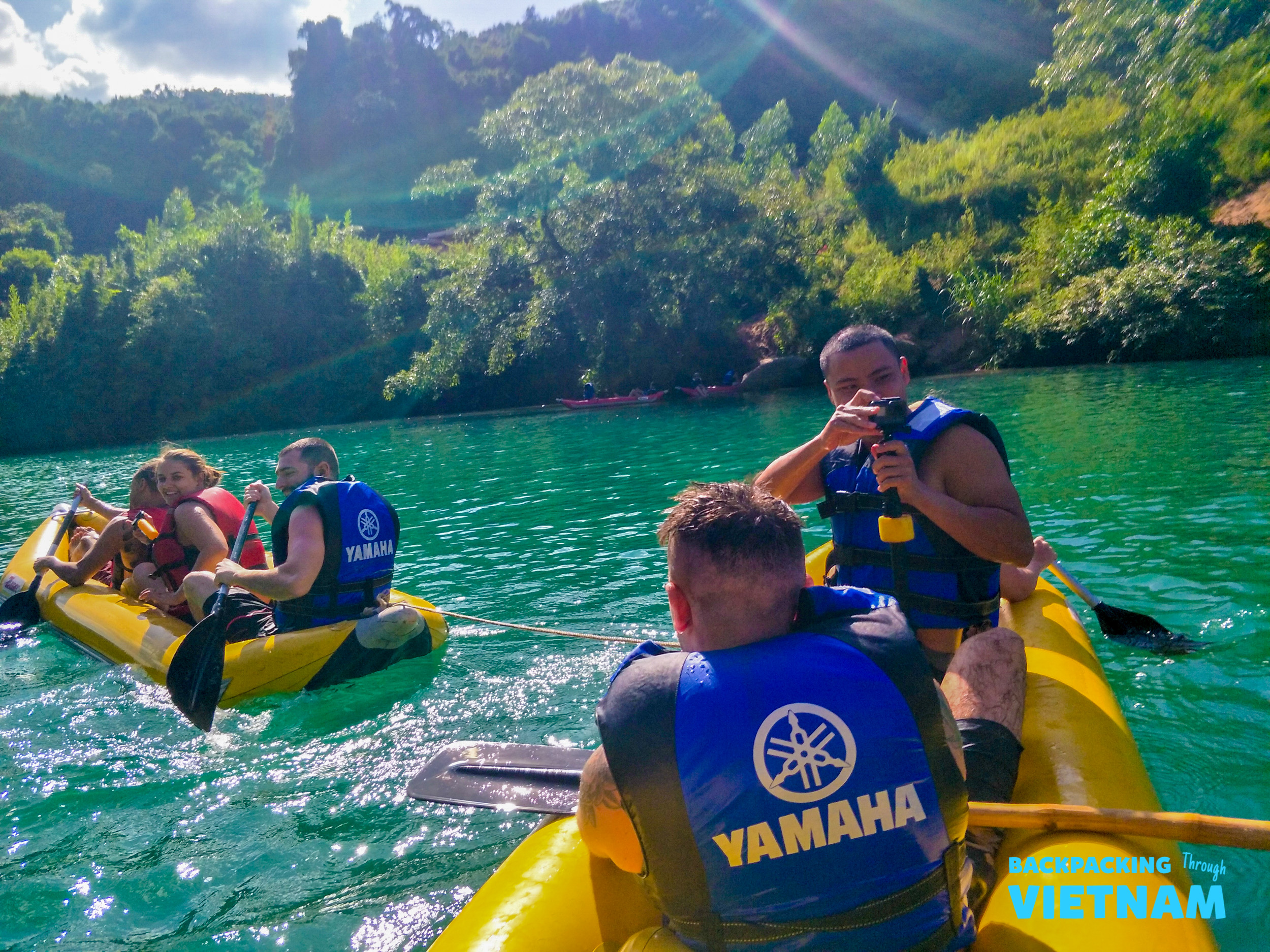 Friends paddle yellow rafts on the stunning emerald water in Phong Nha, Vietnam, enjoying a sunny day.