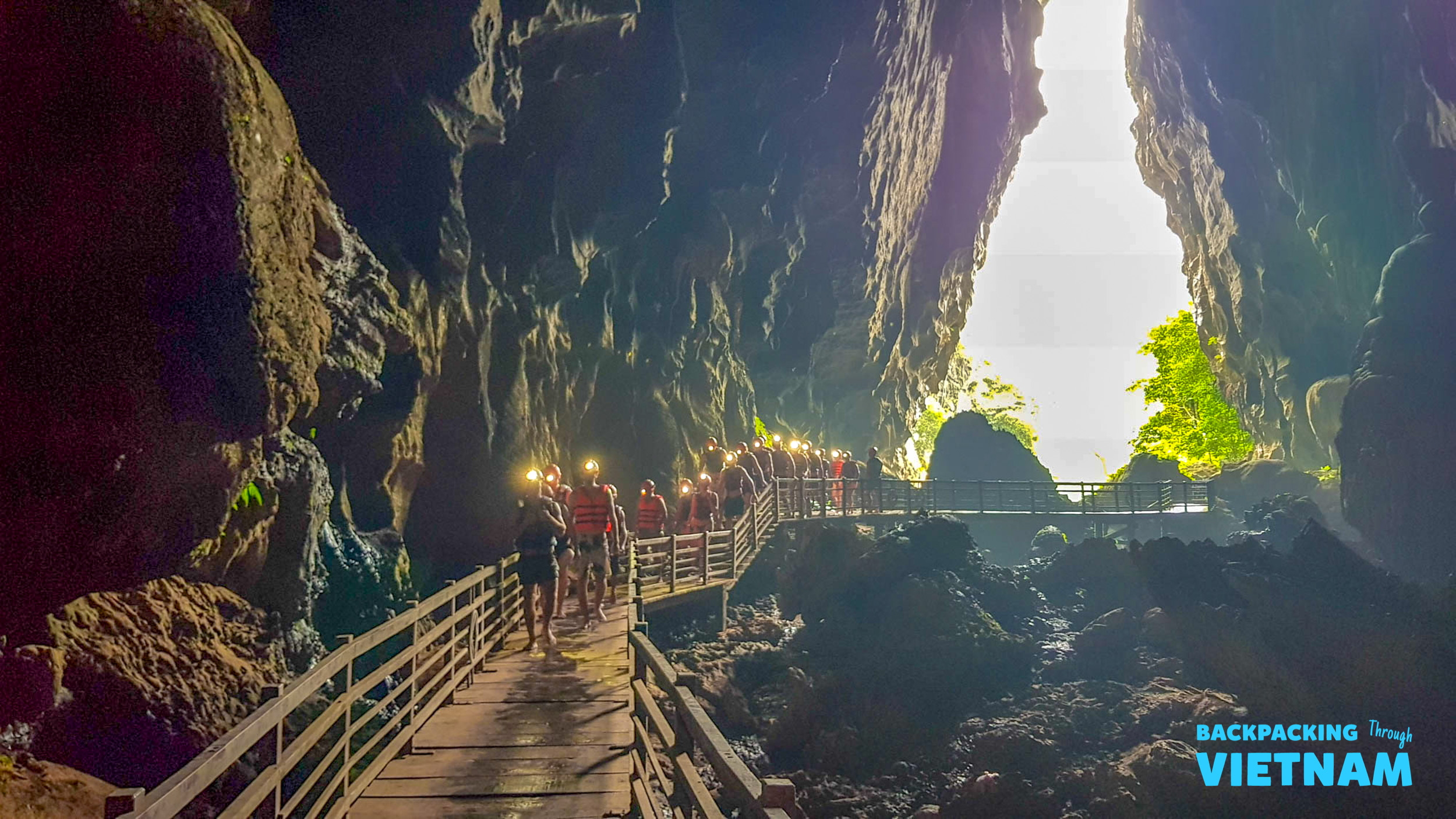 Backpackers with headlamps navigate a wooden walkway through a massive cave in Phong Nha, Vietnam.