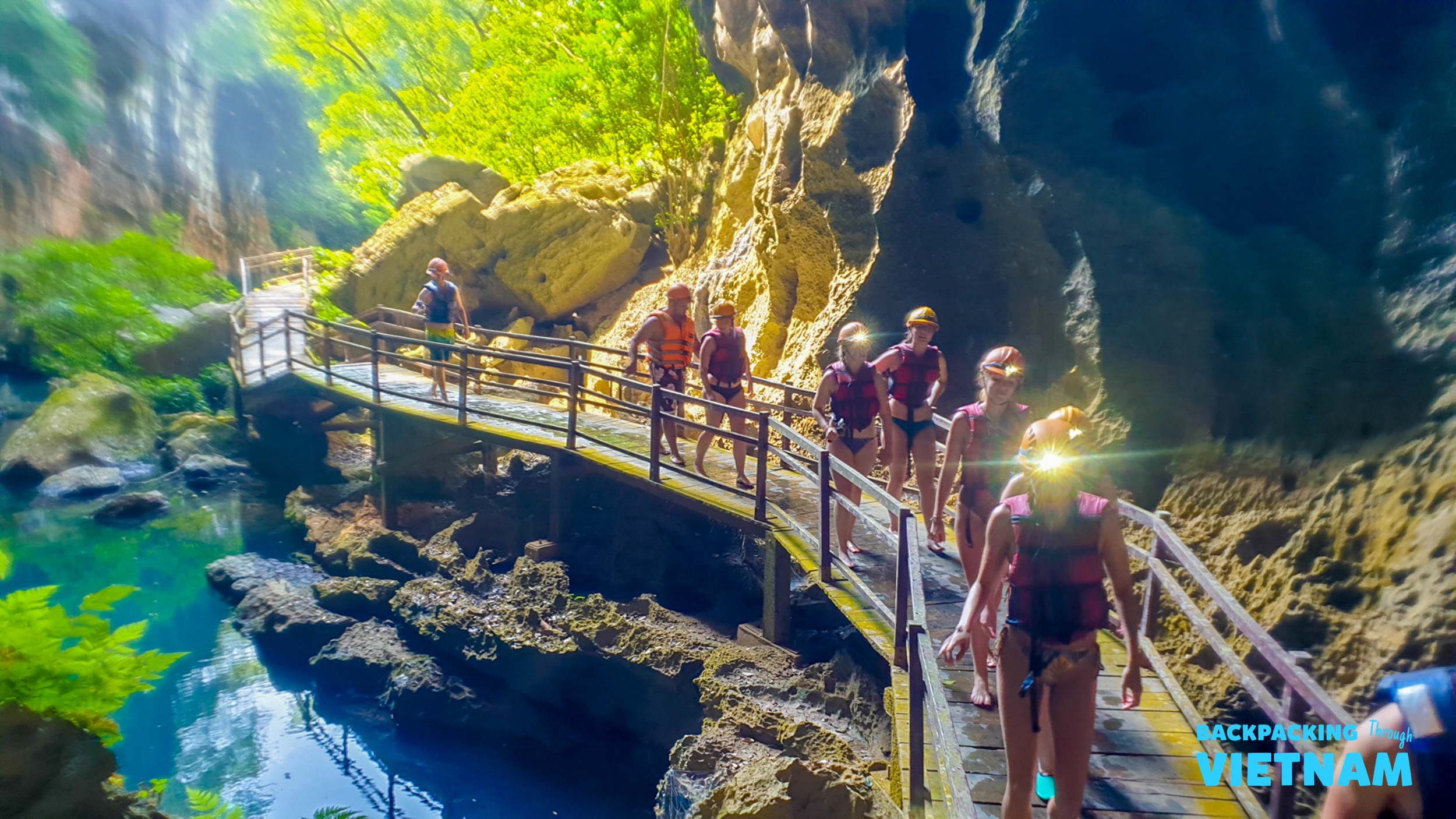 Adventurers explore a stunning cave in Phong Nha, walking a wooden path beside clear blue water.