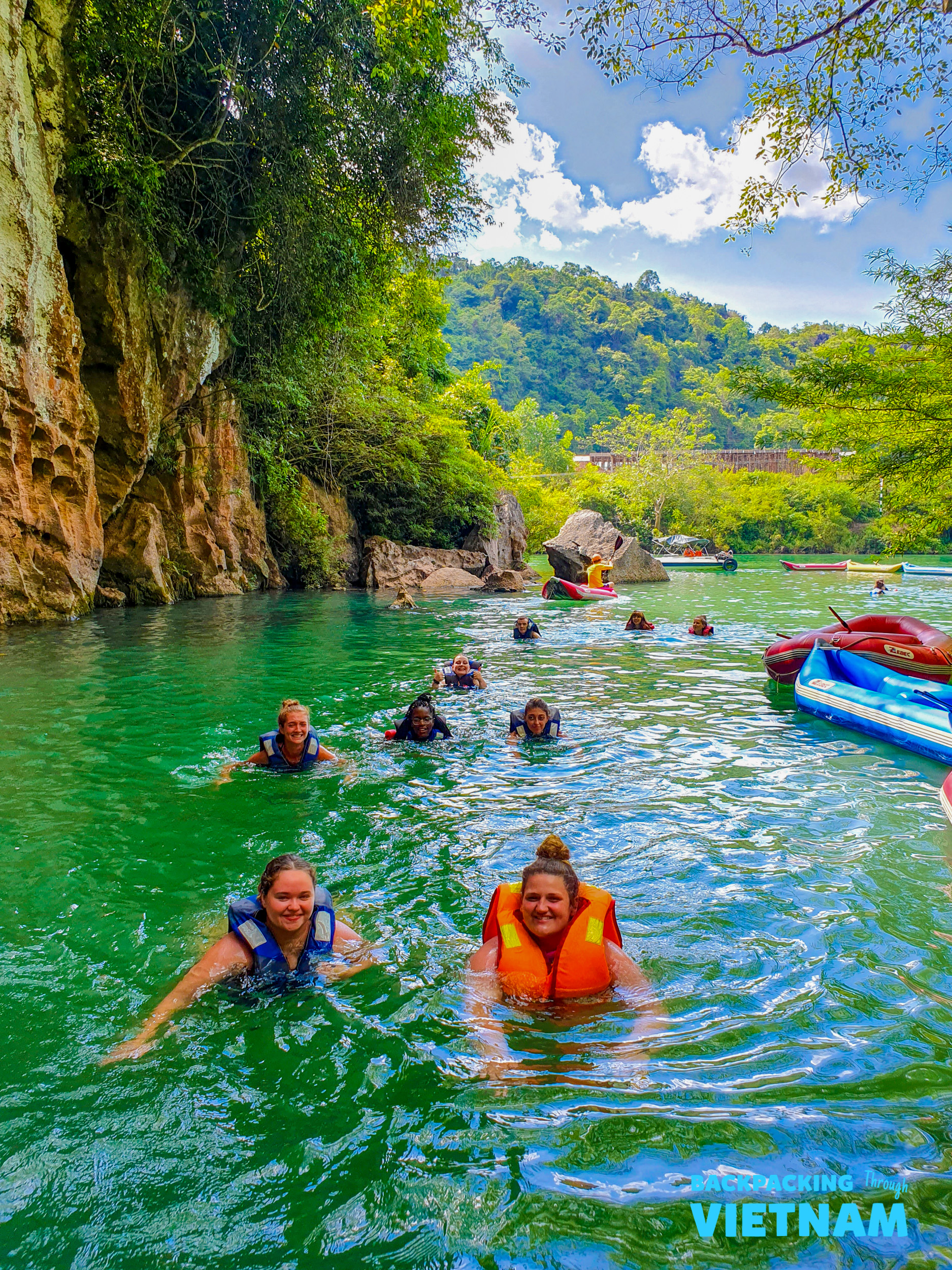 Happy backpackers swim in the refreshing green waters of Phong Nha, surrounded by lush jungle cliffs.