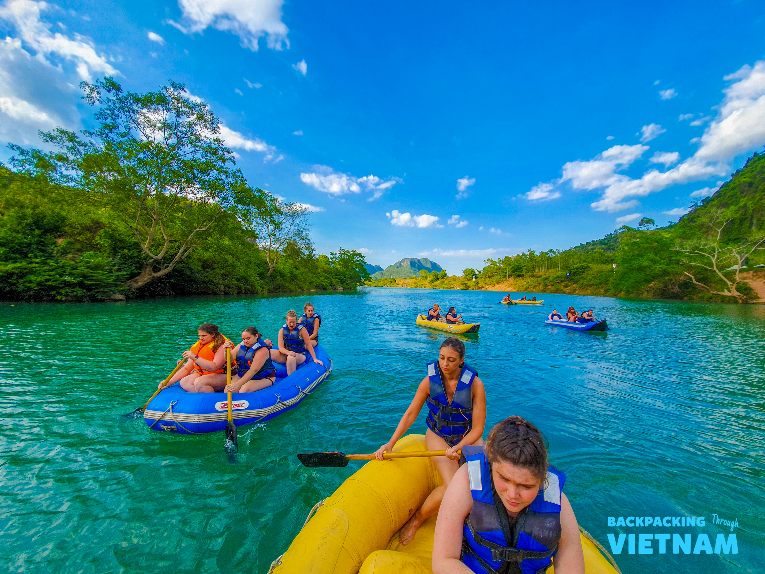 Tourists enjoy paddling on the beautiful turquoise river surrounded by lush green mountains in Phong Nha, Vietnam.