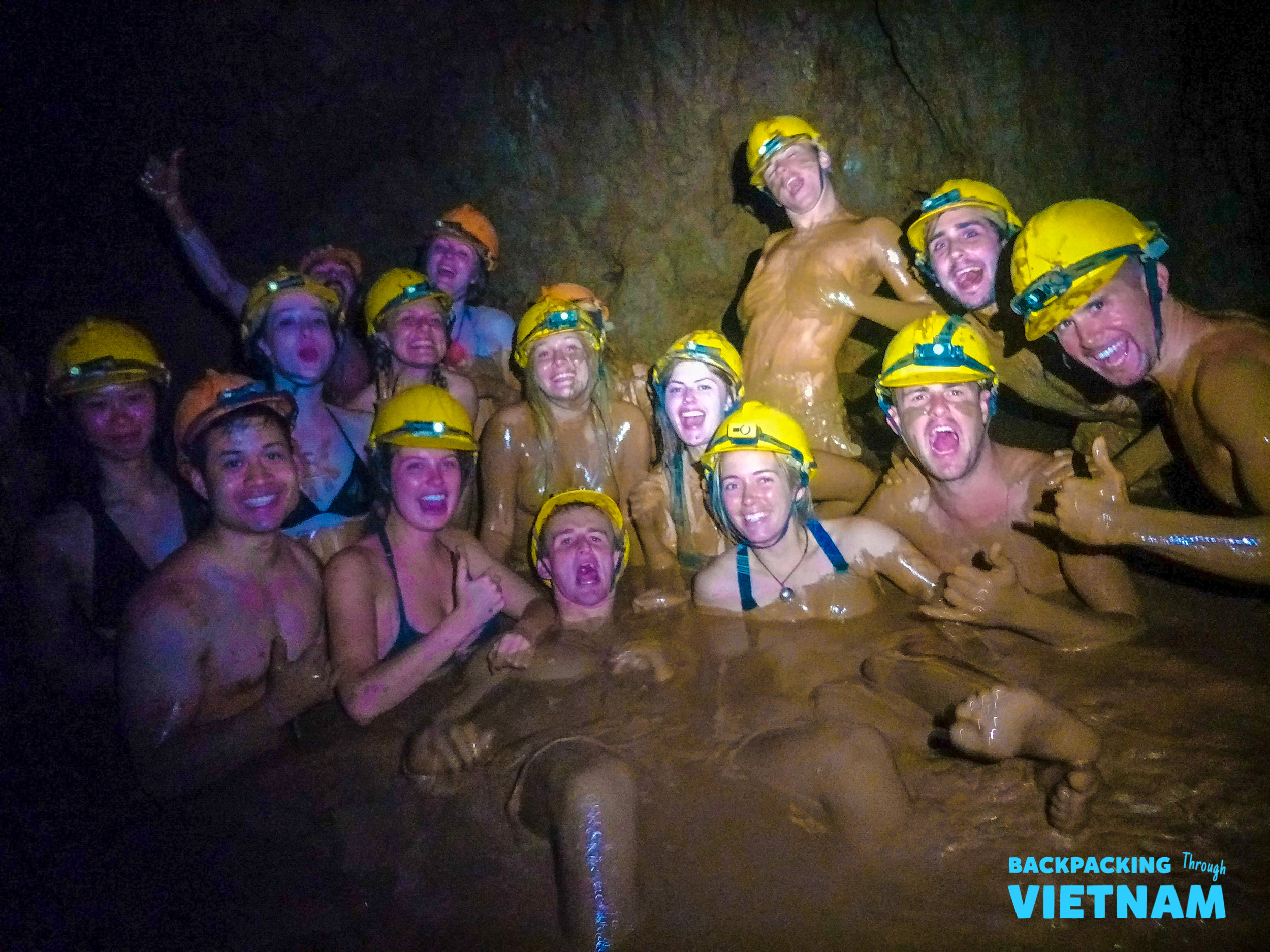 Smiling backpackers covered in mud, enjoying a natural mud bath inside Phong Nha's Dark Cave.
