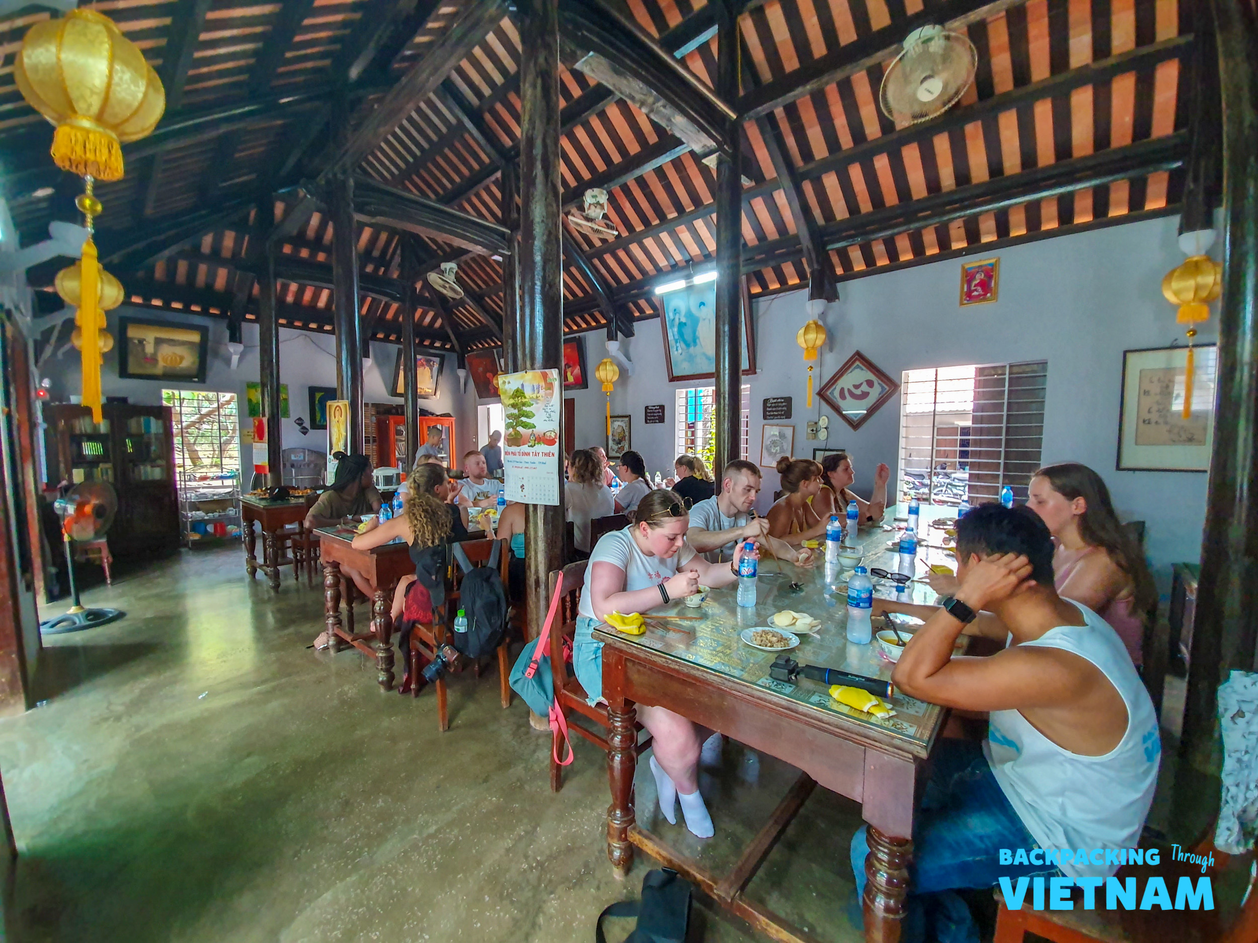 Backpackers enjoy a traditional meal together in a rustic restaurant with wooden beams and lanterns in Hue.