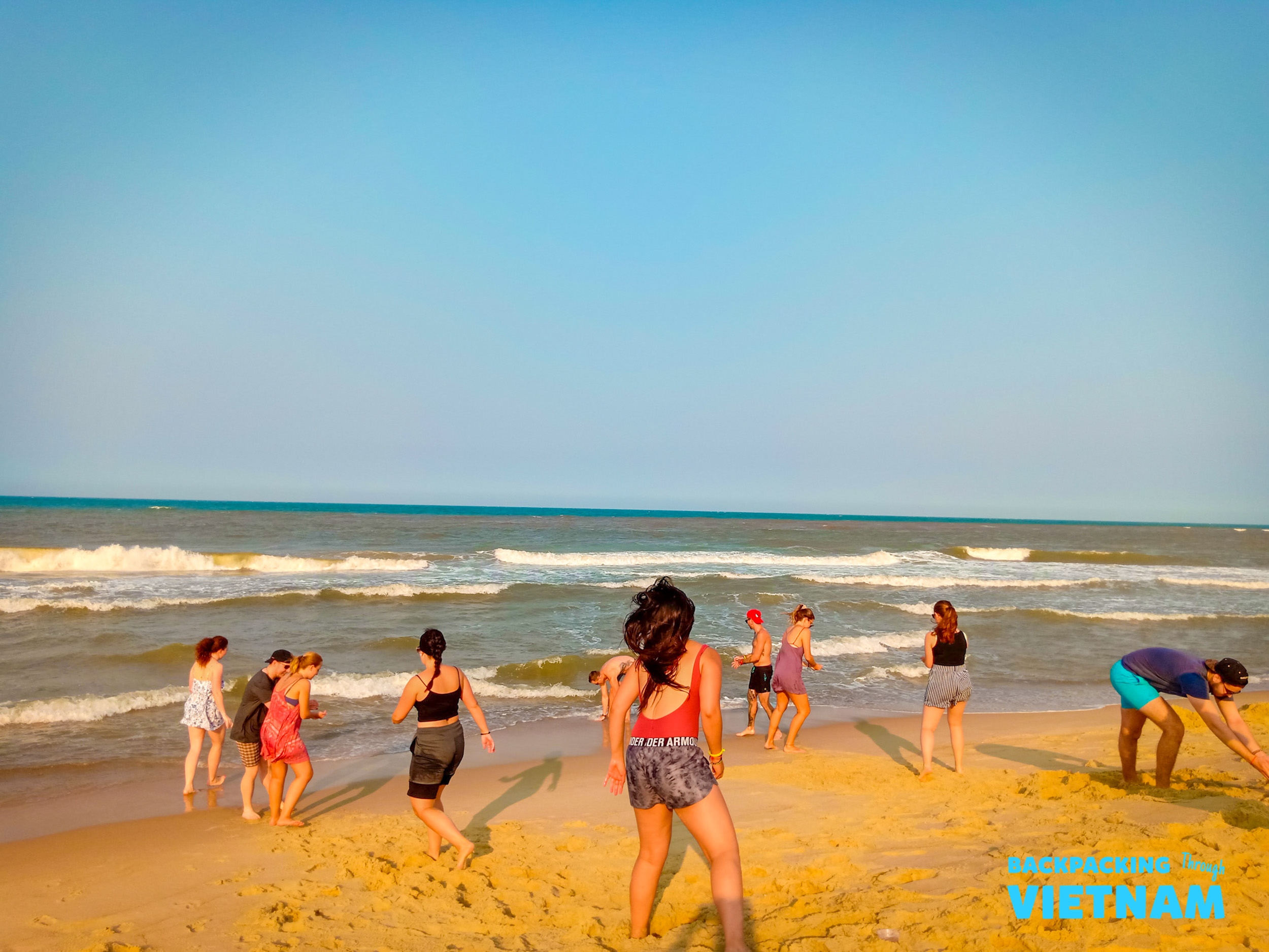 A group of friends enjoying a sunny beach day, walking and playing by the ocean waves in Hue.
