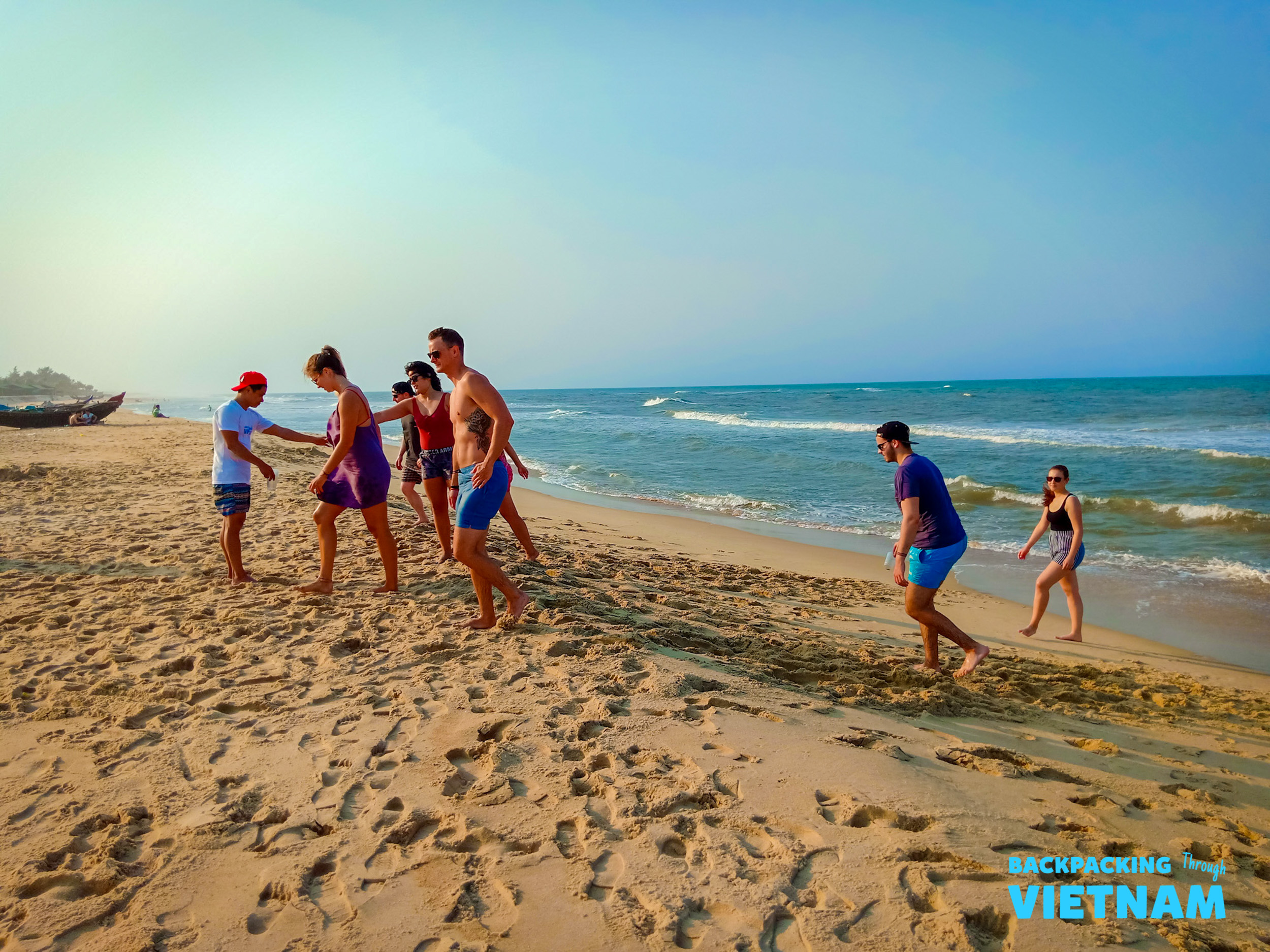 Backpackers enjoy a sunny beach day, walking and playing in the sand on a beach near Hue.