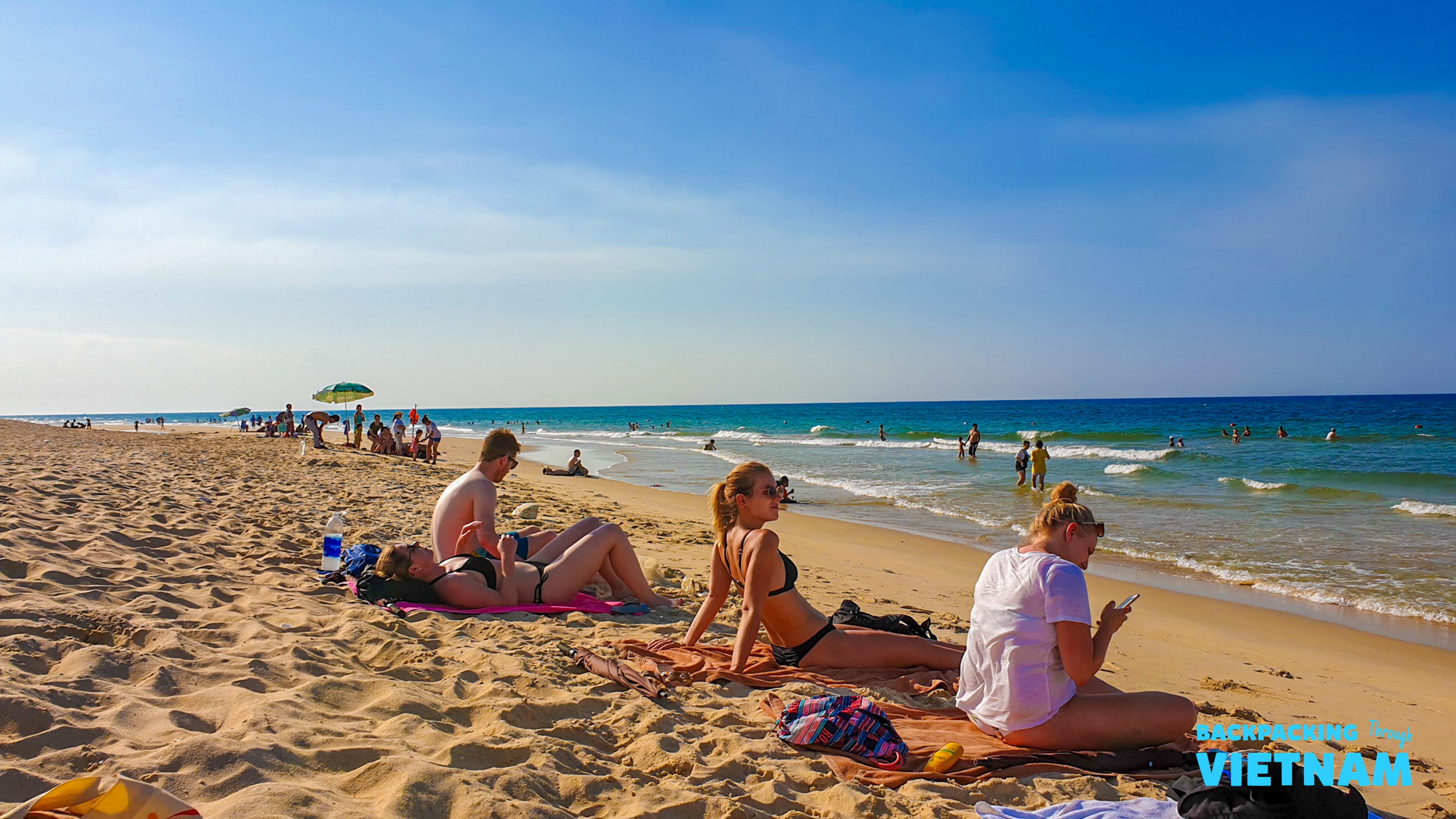 Backpackers relaxing and sunbathing on a beautiful sandy beach under a clear blue sky in Vietnam.