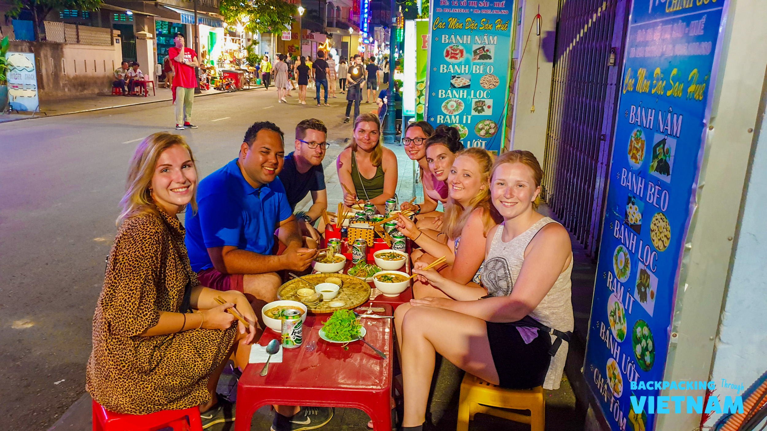 Smiling friends share a traditional Vietnamese street food dinner in the vibrant city of Hue at night.