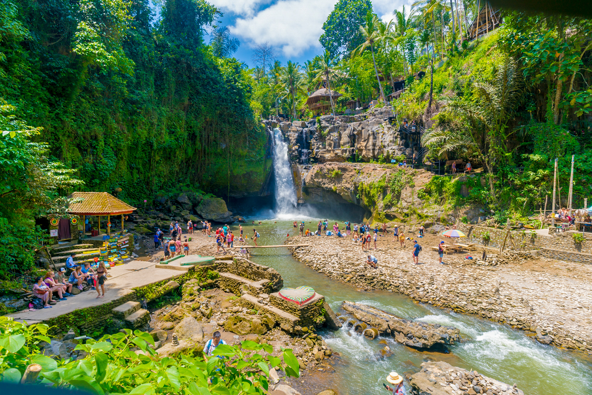 Many tourists gather around a powerful waterfall in Bali, enjoying the lush tropical setting.