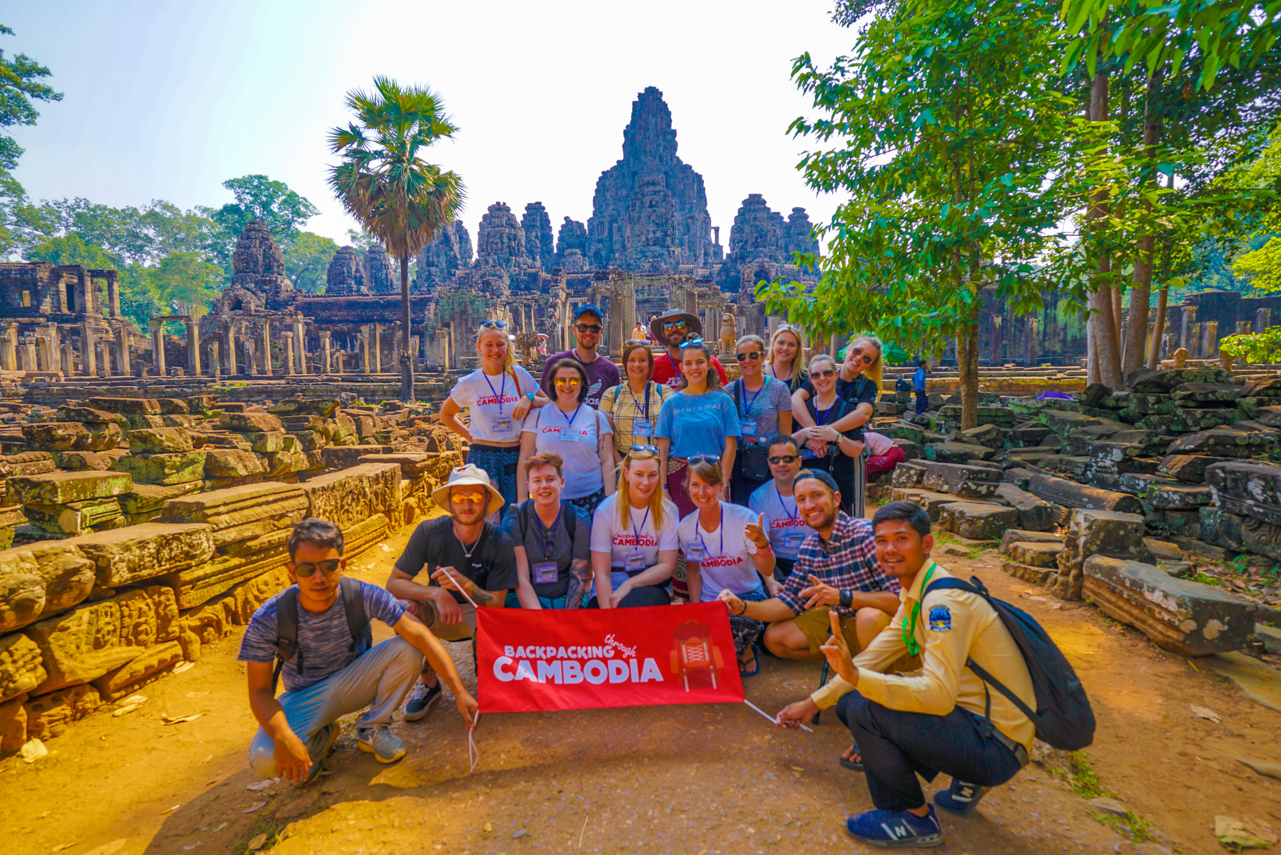 A group of happy backpackers pose with a banner in front of the ancient Bayon temple, Cambodia.