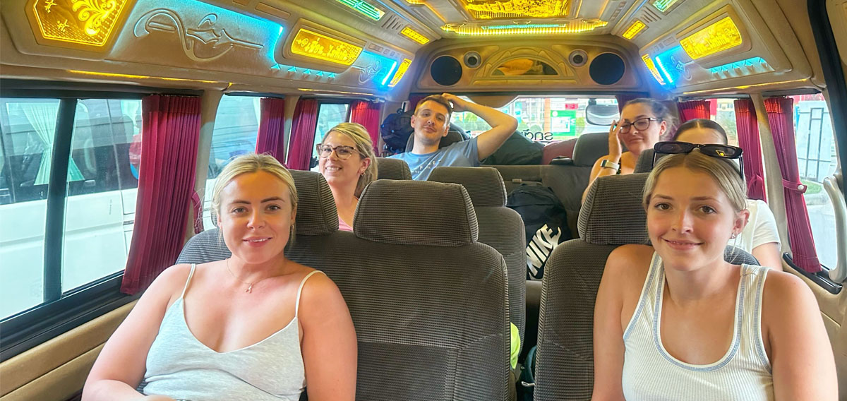 Six happy young travelers smiling inside a colorful, decorated tour van in Thailand.