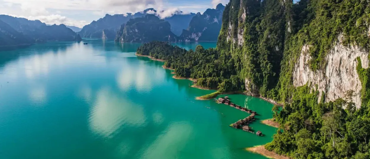 Stunning turquoise lake with floating bungalows and dramatic jungle-covered limestone mountains in Khao Sok National Park.