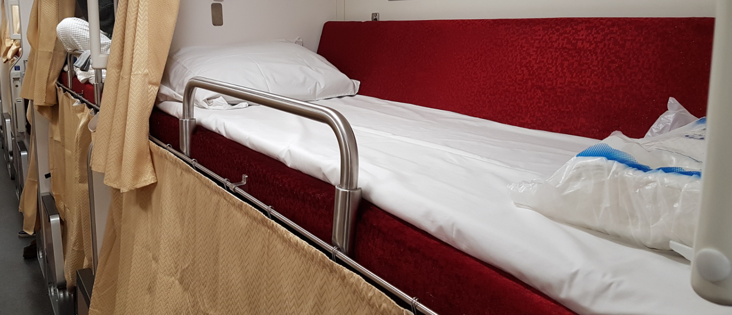 A clean, ready-made bunk bed with a safety rail in a passenger night train cabin.