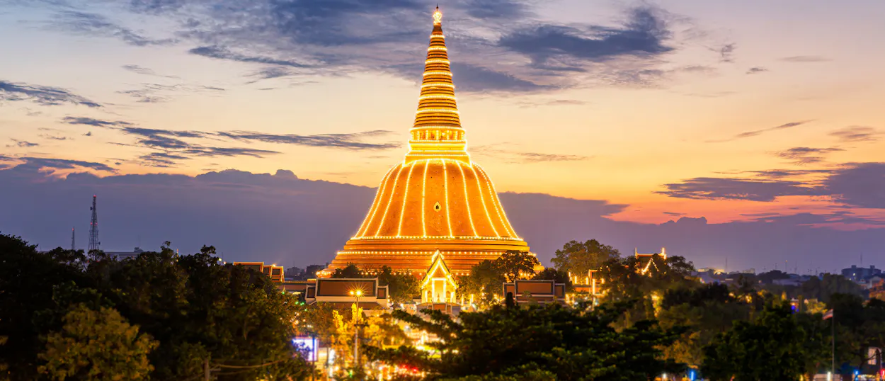 Phra Pathom Chedi, a grand golden stupa, glows brightly against a colorful sunset sky in Thailand.