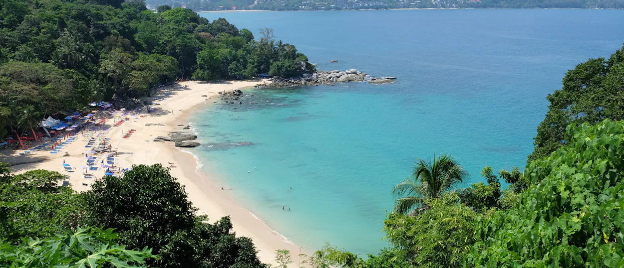 Serene Phuket beach with sun loungers on white sand and calm turquoise ocean.
