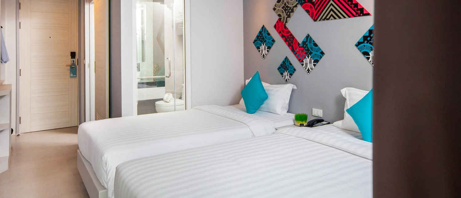 Bright hotel room in Phuket featuring two single beds with white linens and blue pillows.