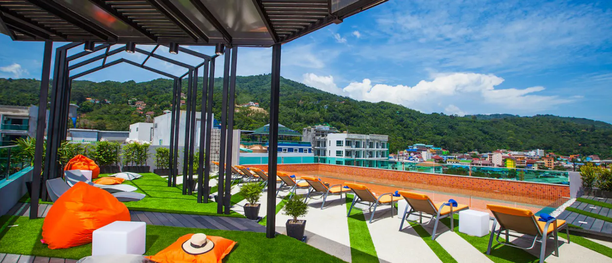 Relaxing rooftop pool deck in Phuket with lounge chairs, bean bags, and lush green hills.