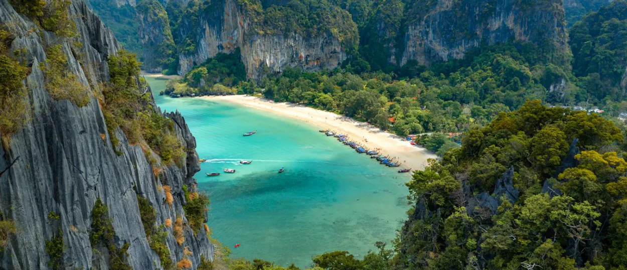 Aerial view of Railay Beach in Thailand, with turquoise water, white sand, and towering limestone cliffs.