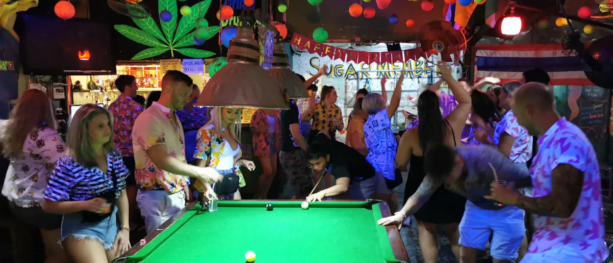 Backpackers enjoy a lively night out, playing pool and dancing in a vibrant bar in Thailand.