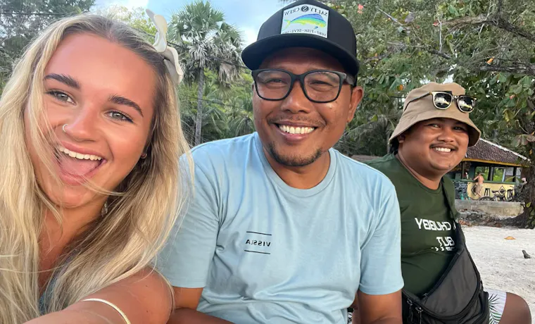 Three happy friends smiling for a selfie on a sandy beach in Bali.