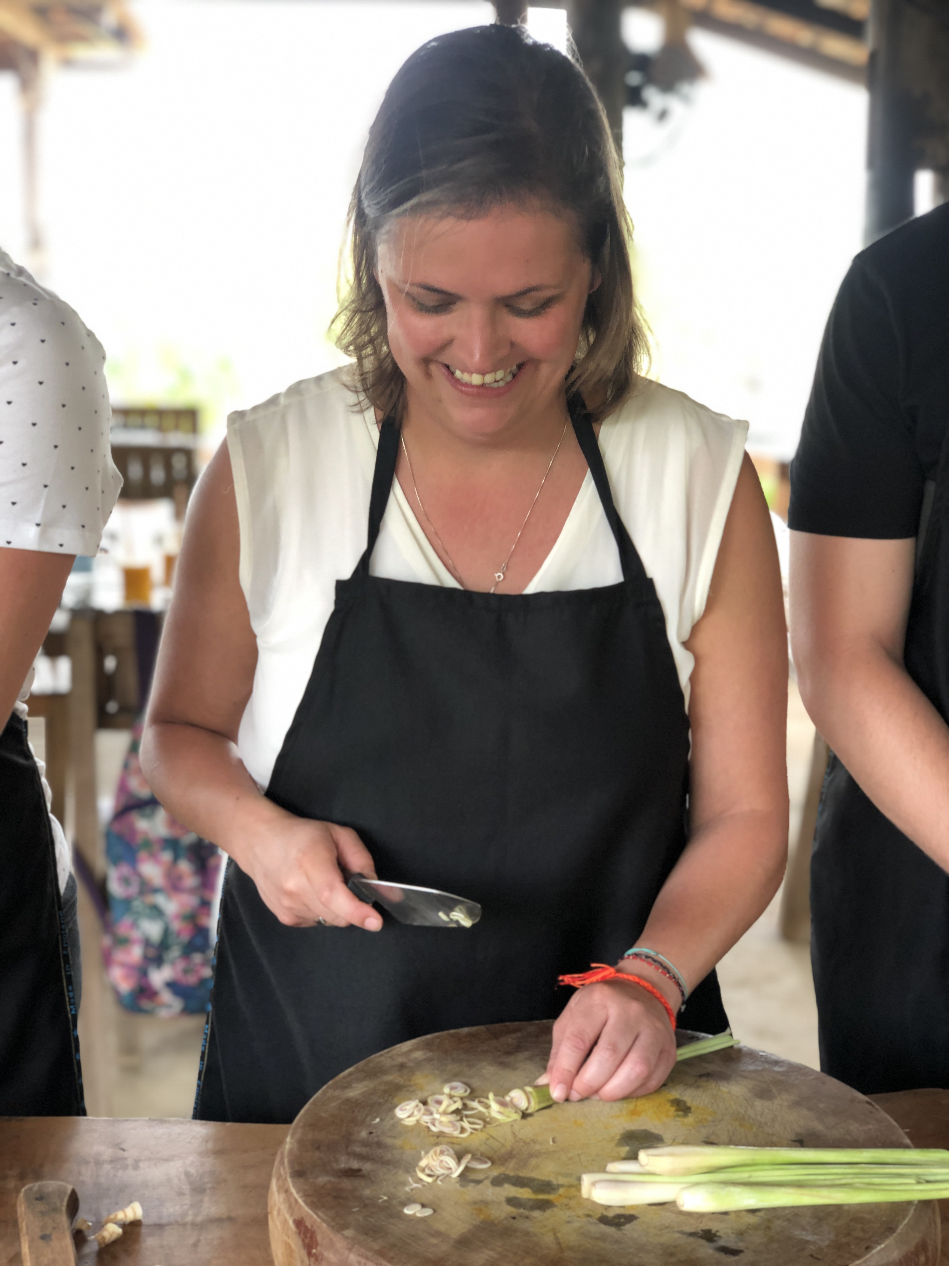 Happy woman in a cooking class chopping lemongrass on a wooden board in Cambodia.