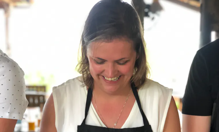 Happy woman in a cooking class chopping lemongrass on a wooden board in Cambodia.
